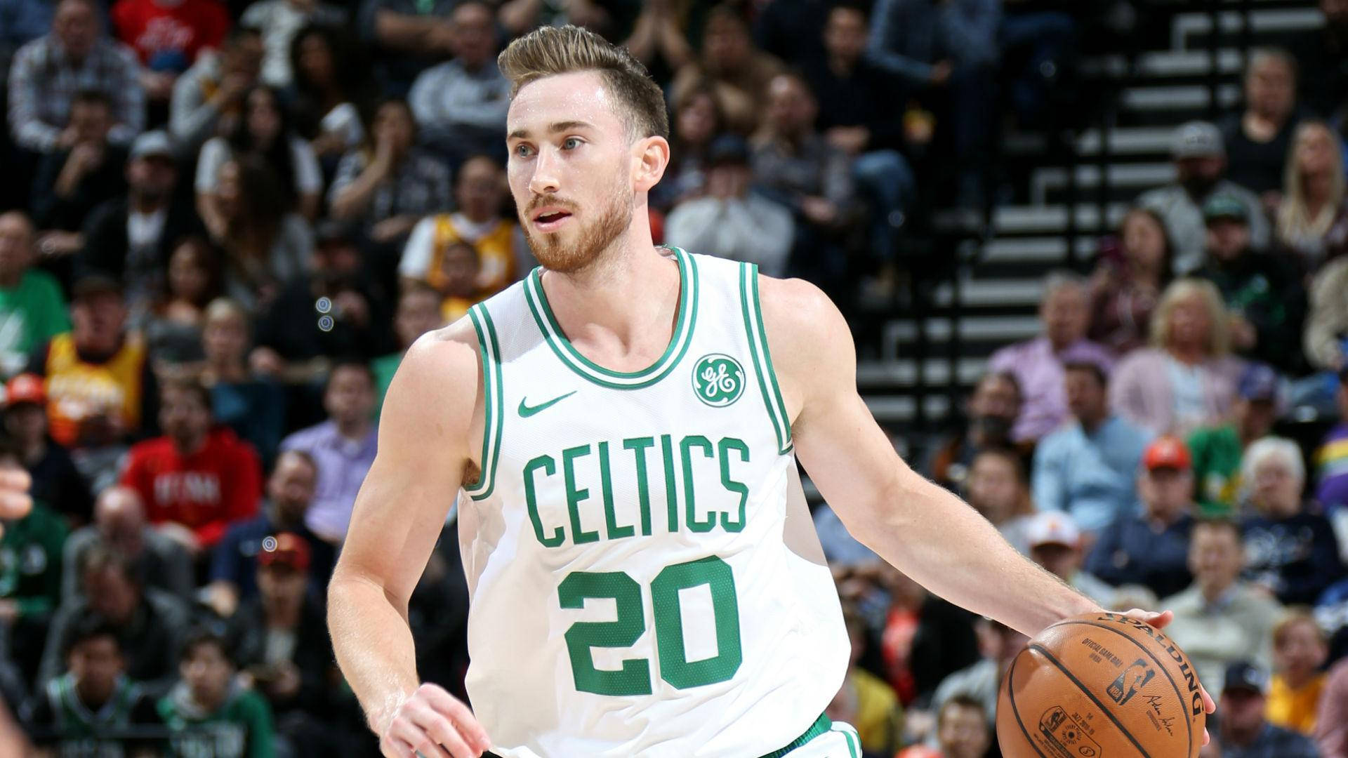 戈登·海沃德NBA塞爾提克隊前進 壁紙 — 一位身穿白色和綠色球衣的波士頓塞爾特人籃球運動員在比賽中運球，背景是模糊的人群。