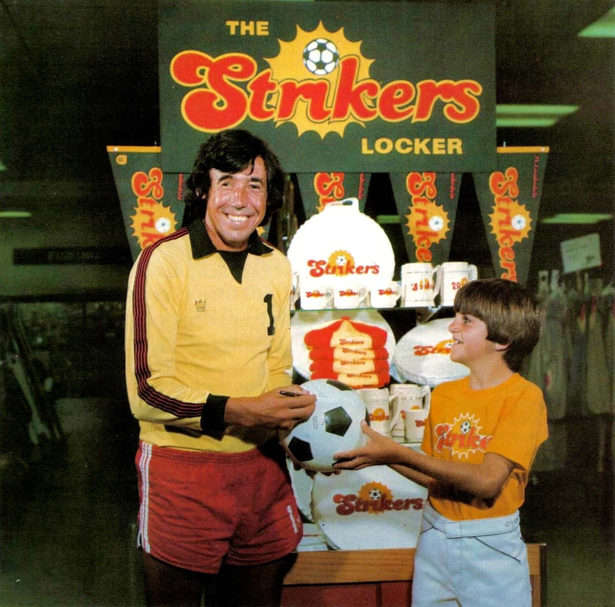 足球員與男孩在Strikers Locker商品展示架前拿著球。