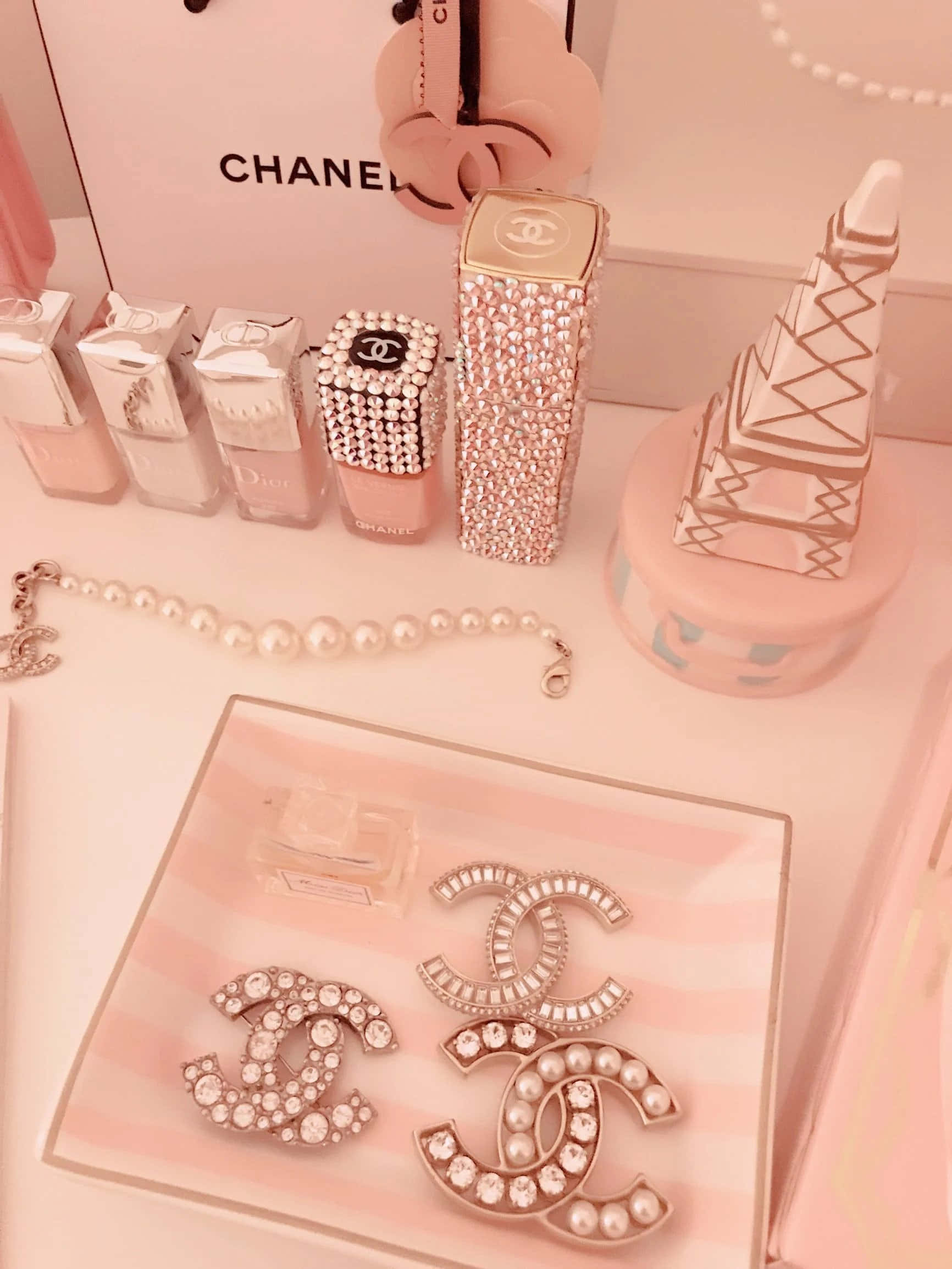 成為經典。 壁紙 — 柔和溫暖燈光下的粉紅色梳妝檯展示，配有Chanel和Dior化妝品、珍珠首飾和標誌性Logo配件。