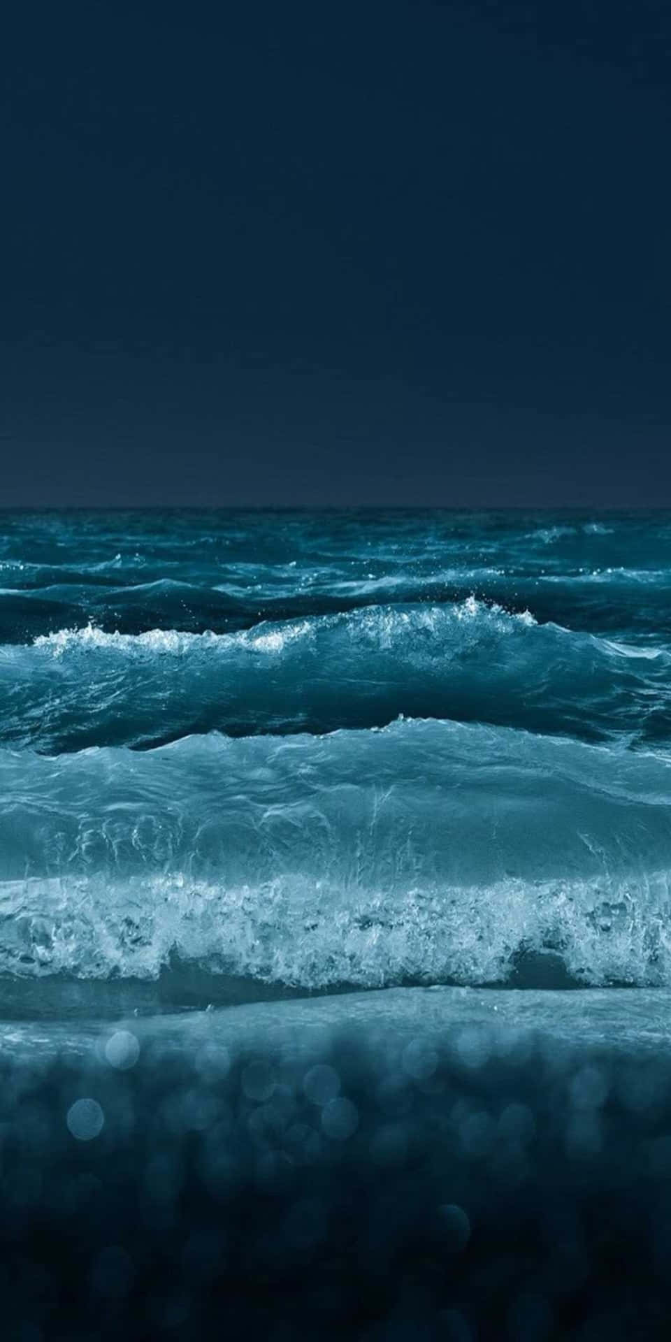 藍綠色海洋波浪在夜間破碎，黑暗天空和散景前景