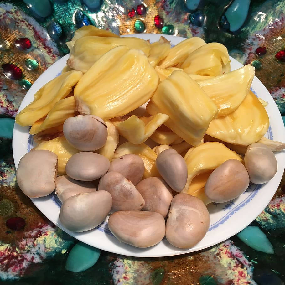 白色碟子盛載菠蘿蜜果肉和種子，置於彩色珠子背景上。