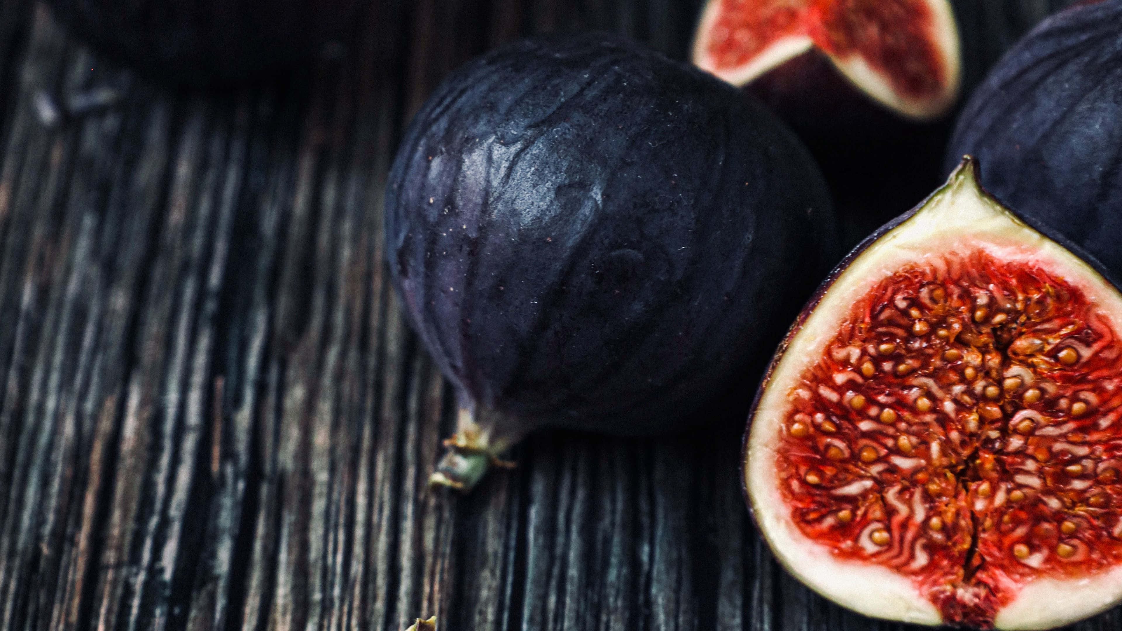 Purple Figs 桌布 壁紙 — 成熟的深紫色無花果，多汁的紅色內部，放在風化的木質表面上。