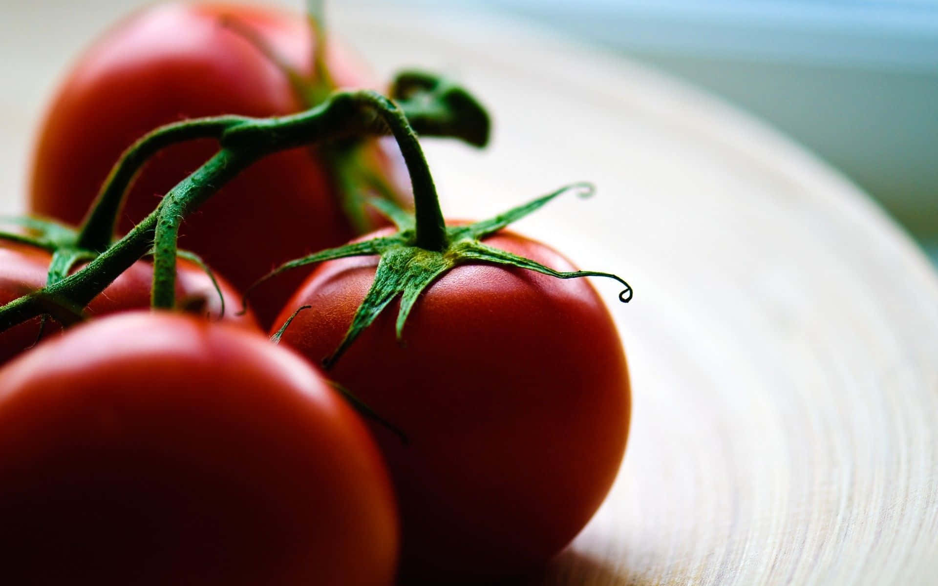 tomato 桌布 壁紙 — 成熟的紅色番茄仍連著綠色藤蔓，放在淺色木質表面上，光線柔和自然。