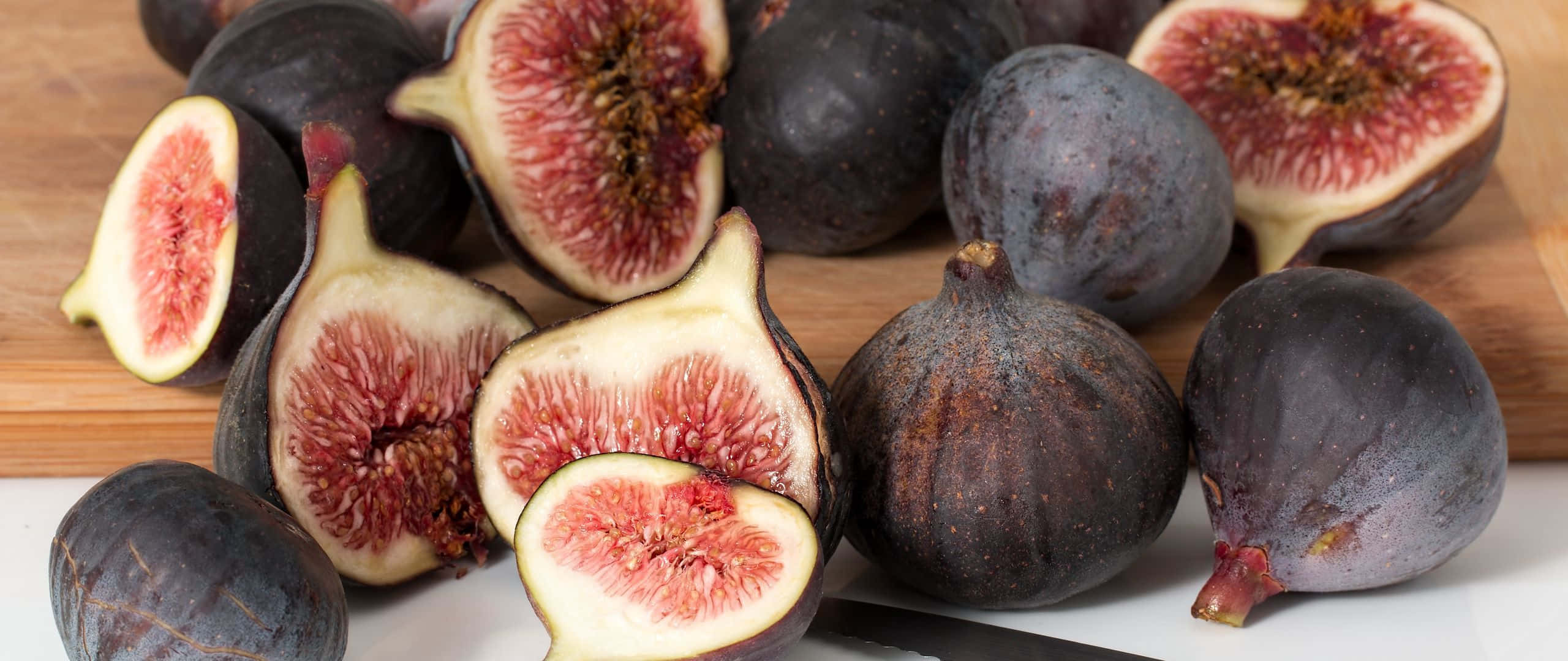 Purple Figs 桌布 壁紙 — 成熟的紫色無花果切開，露出粉紅色果肉，放在木砧板上。