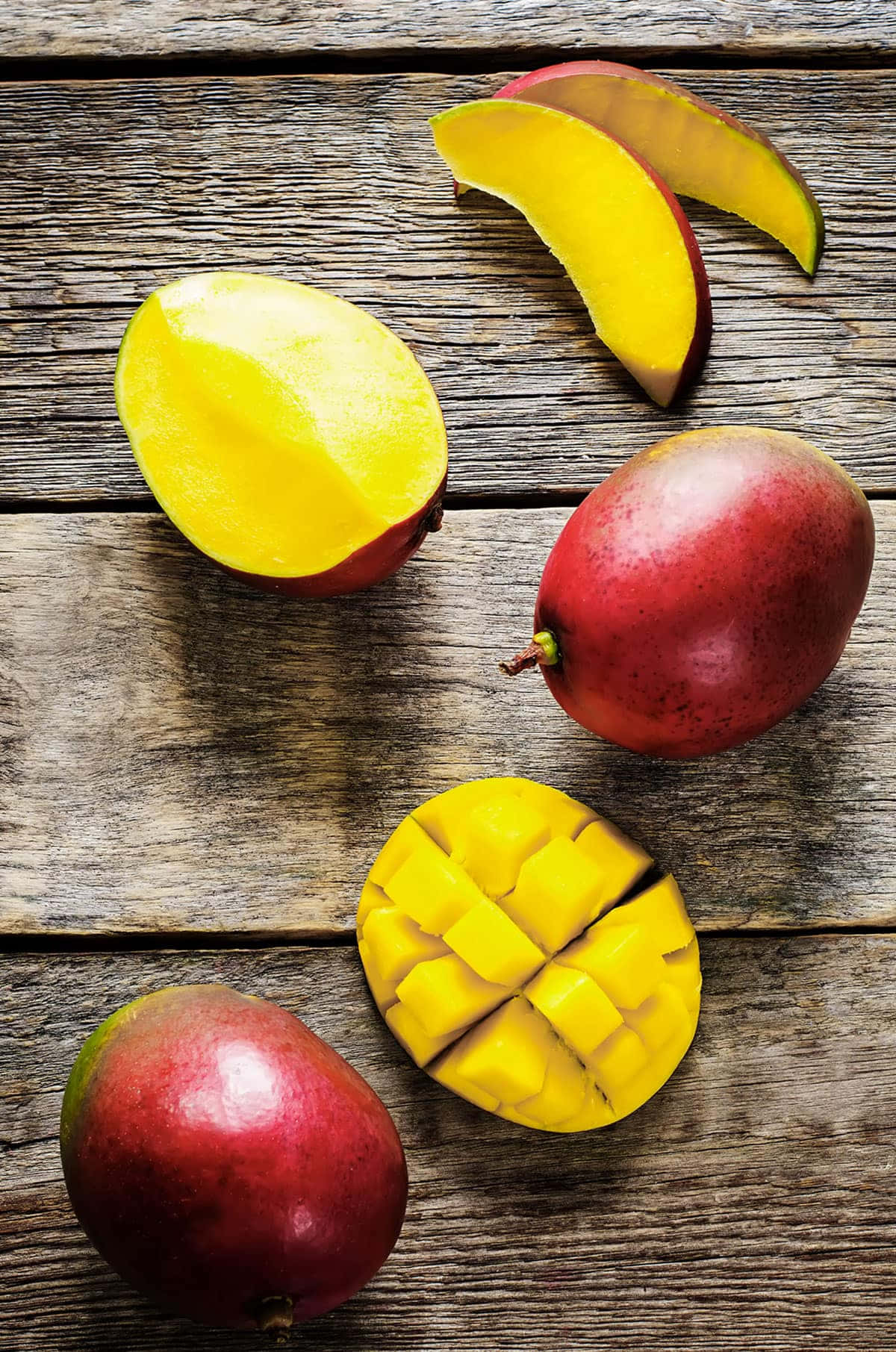 Mango 桌布 壁紙 — 成熟的芒果切片和完整芒果放在風化的木質表面上，展現出鮮黃色的果肉和深紅色的果皮。