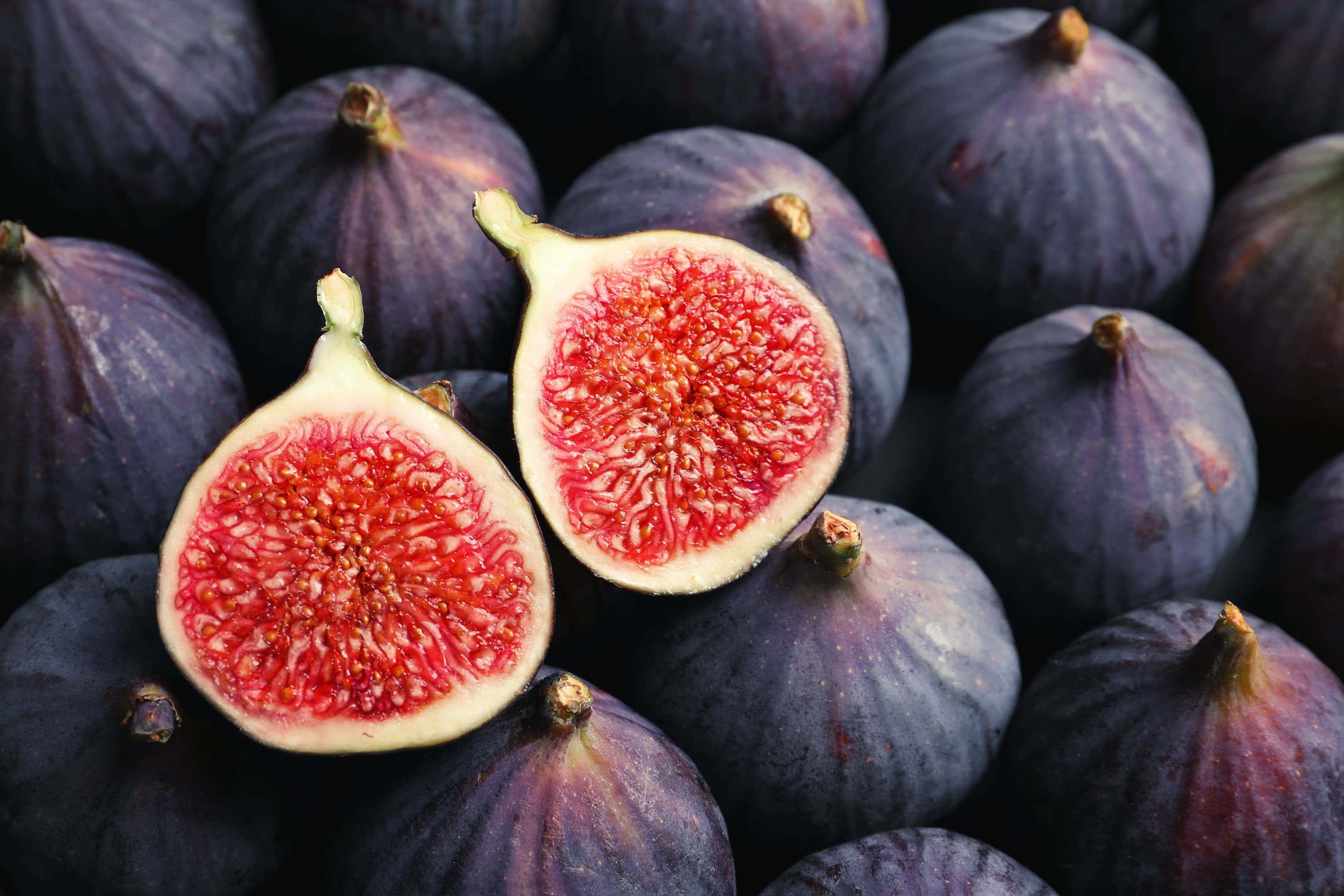 Purple Figs 桌布 壁紙 — 成熟紫色無花果的特寫，其中一個切開一半，露出多汁的紅色果肉。