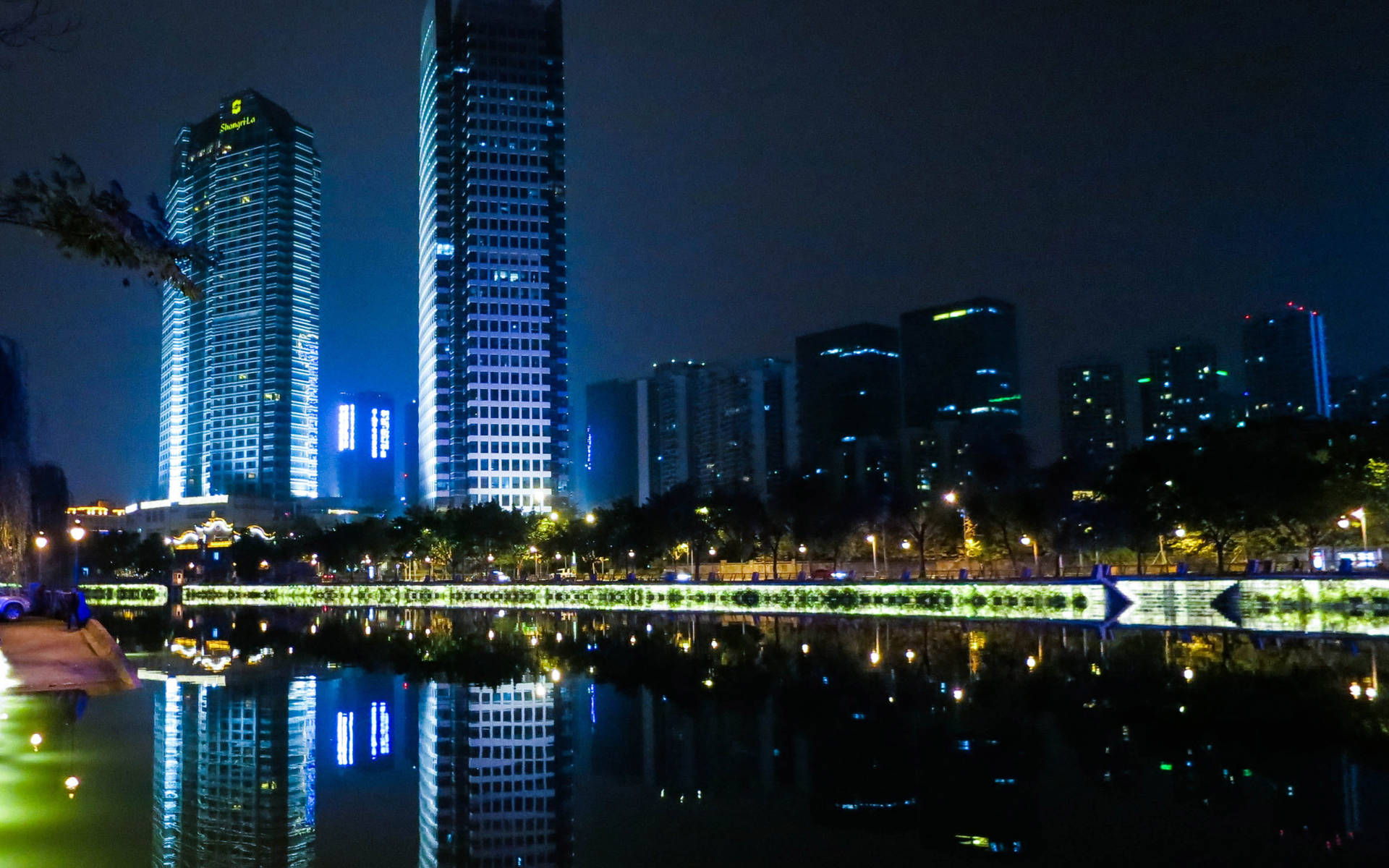 夜晚城市天際線，燈火通明的摩天大樓倒映在寧靜的湖中。