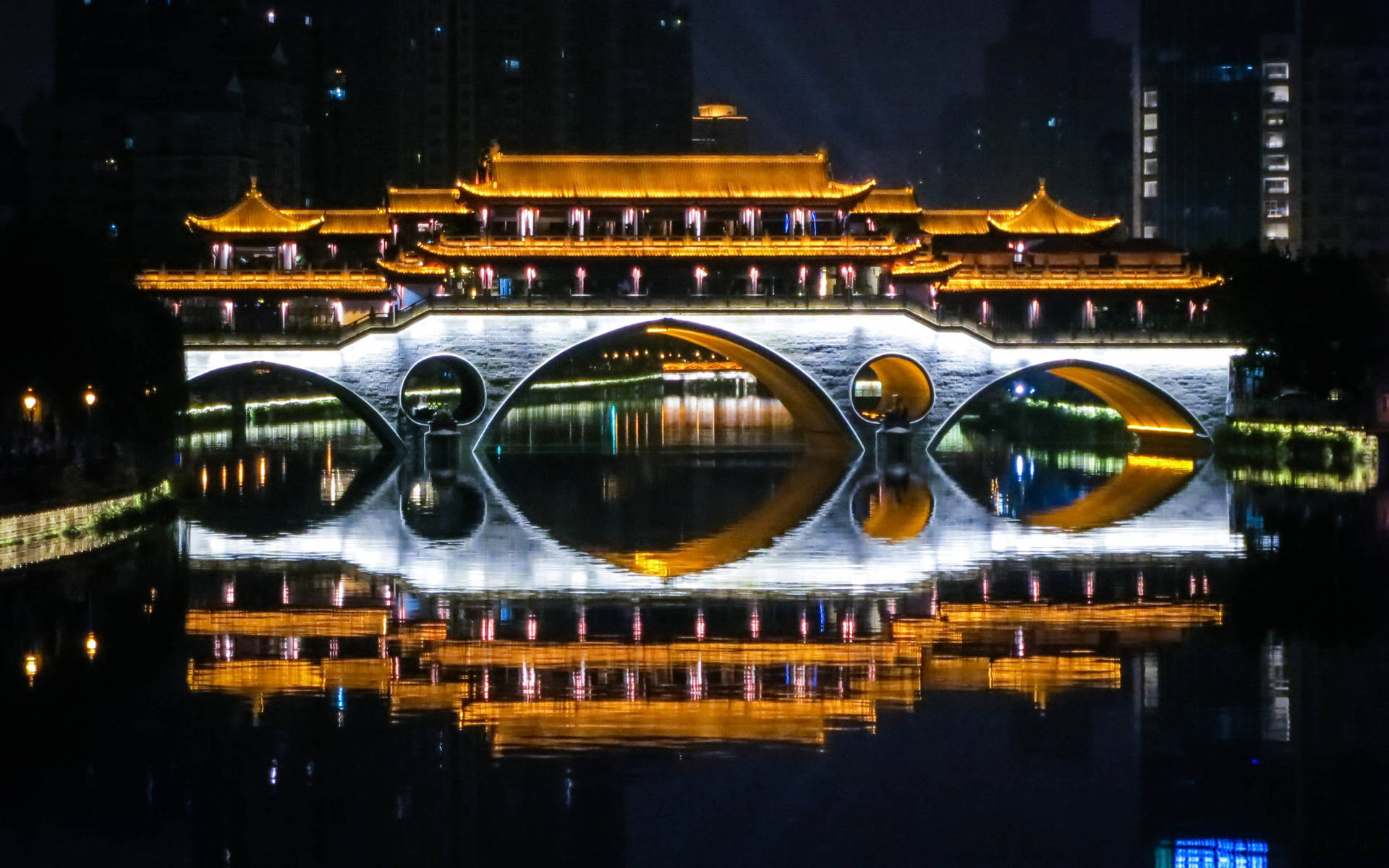 夜晚城市中，燈光照亮的傳統中式橋樑在平靜水面上倒映。