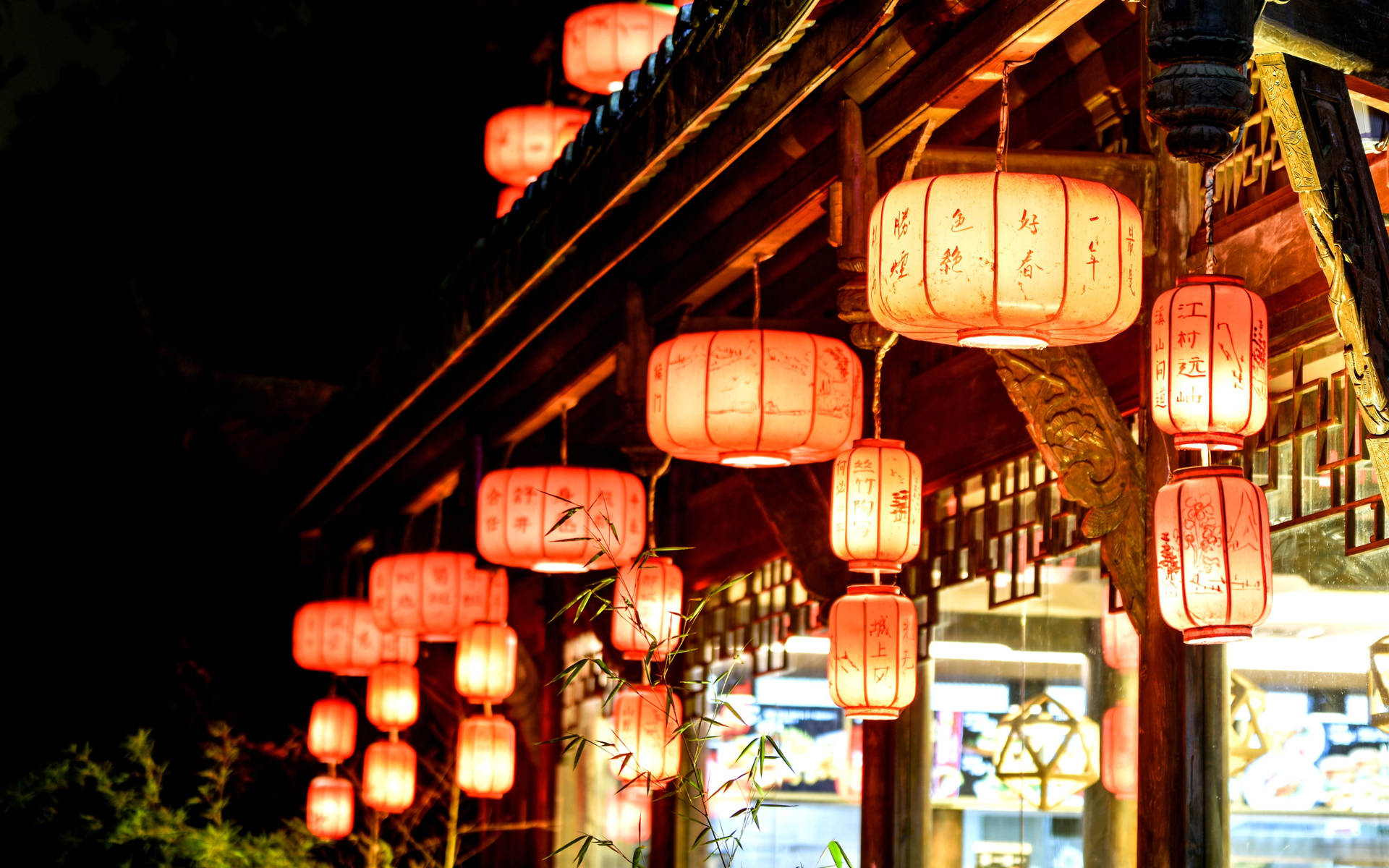 傳統紅色燈籠在夜間照亮木建築，前景有竹子。