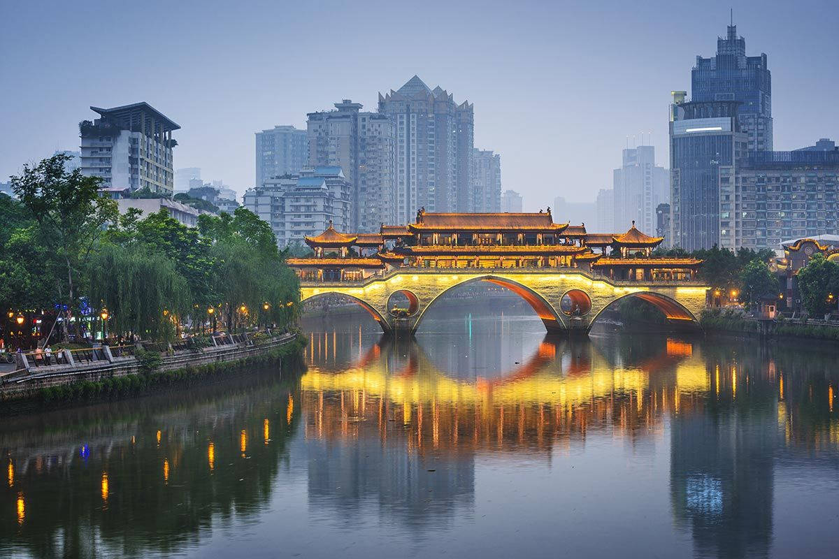 黃昏時分亮燈的歷史中國橋樑，河中有倒影，周圍是城市建築。