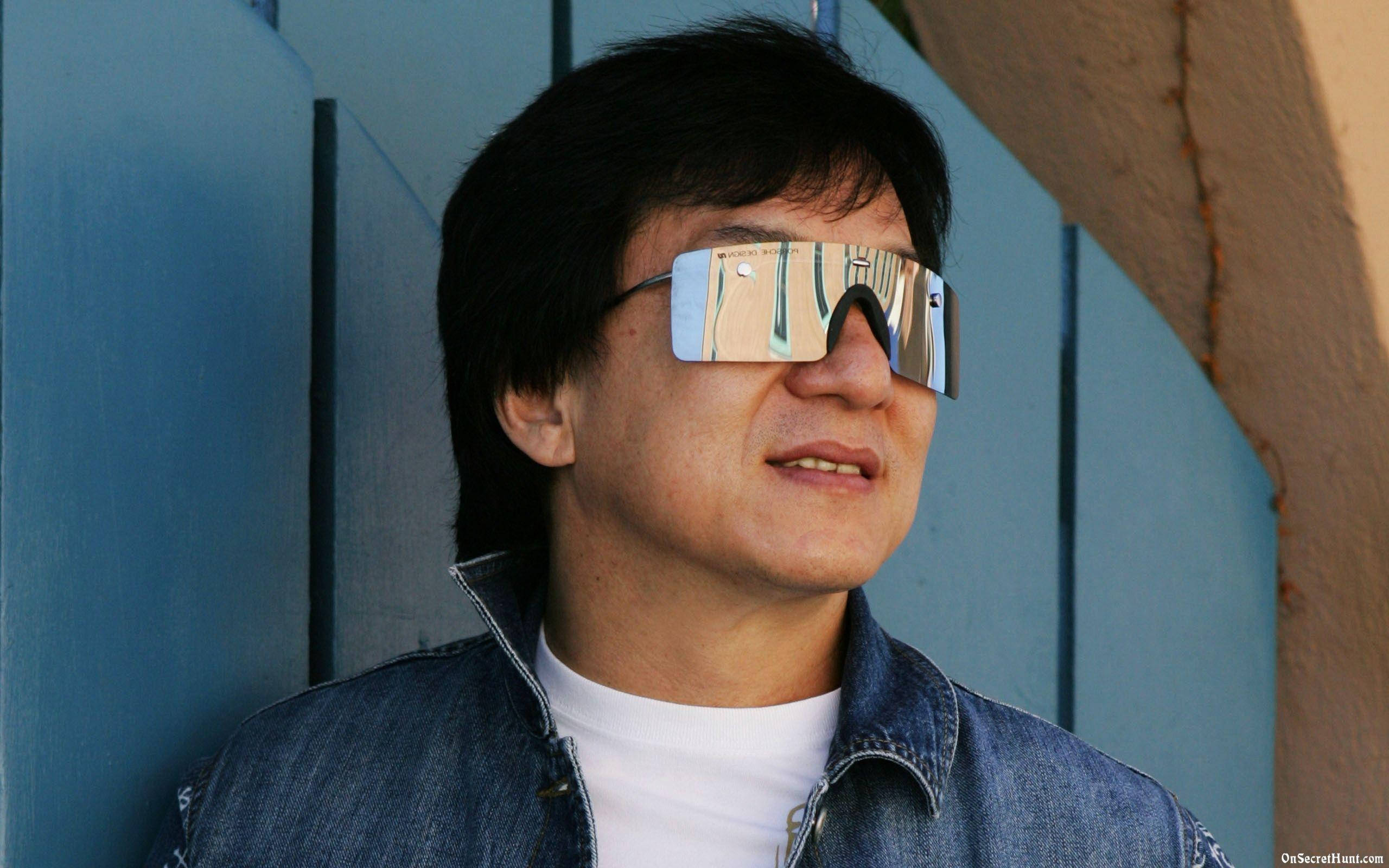 成龍銀色太陽眼鏡 壁紙 — 一名深色頭髮的男子戴著反光太陽眼鏡和牛仔外套，靠著藍色木牆。