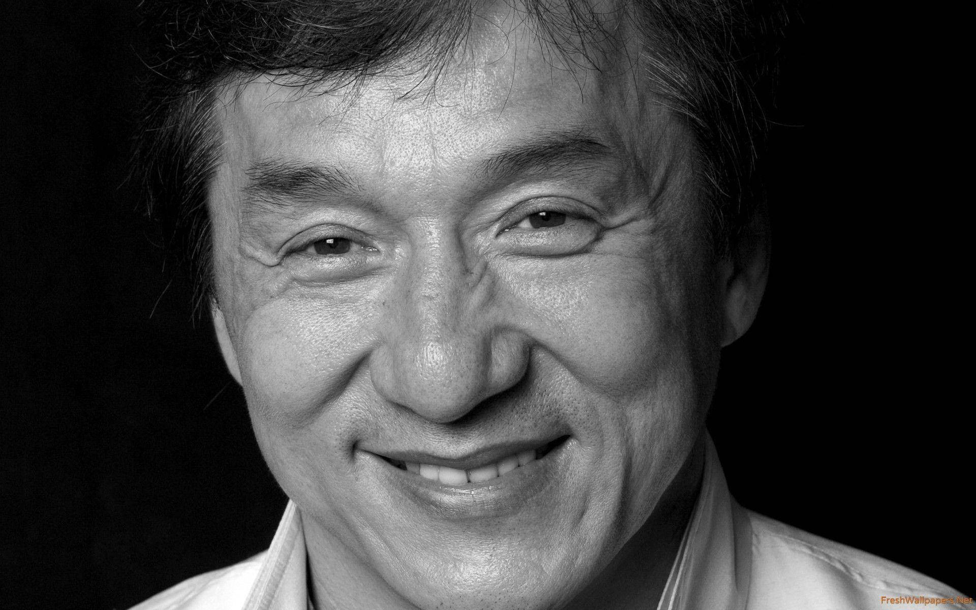 成龍黑白近照 壁紙 — 一個微笑男士的黑白特寫肖像，眼神富有表現力，帶有溫暖的皺紋，背景為深色。