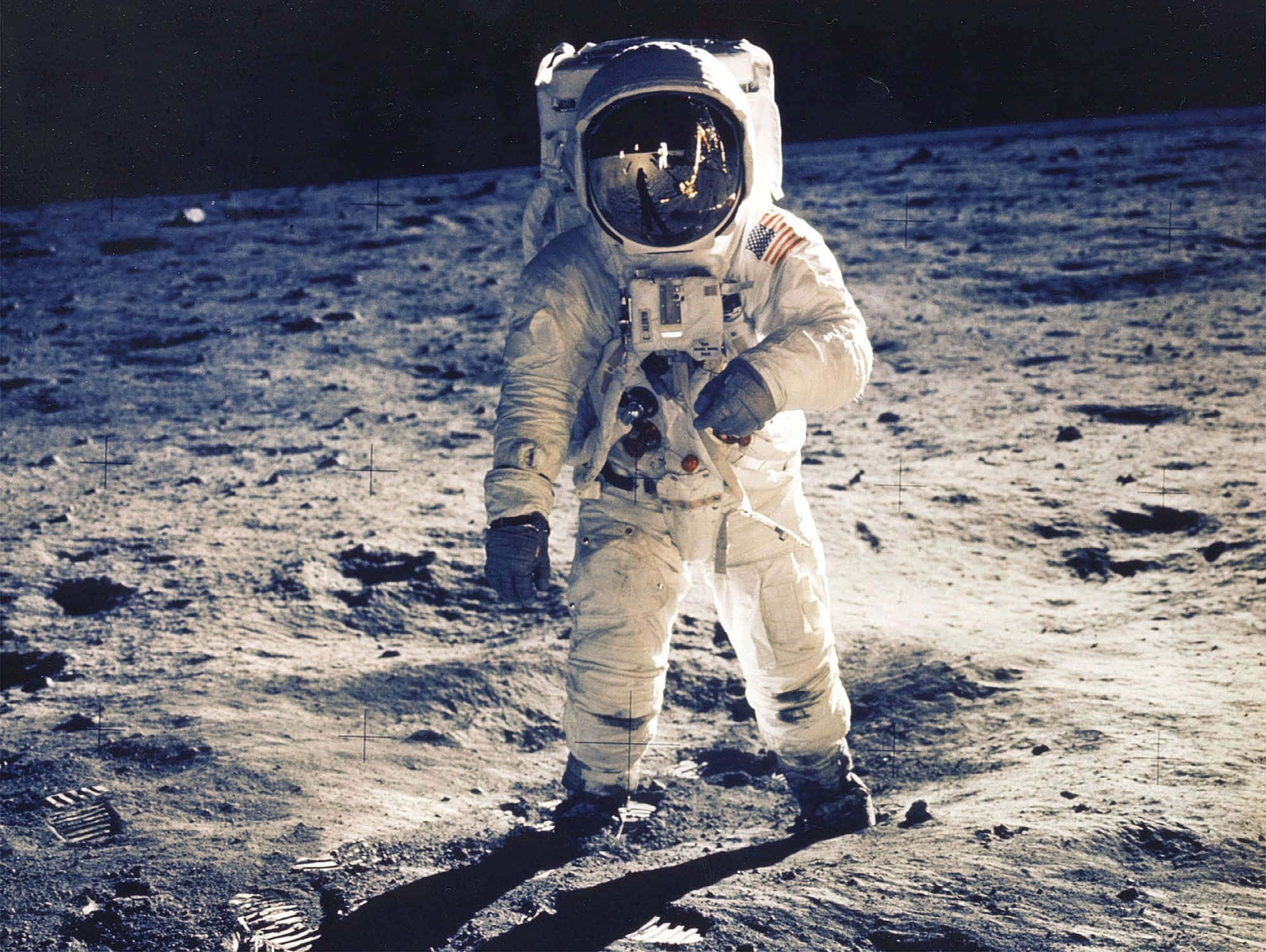我們宇宙的壯麗 壁紙 — 一名身穿白色太空衣的太空人站在月球灰色的塵埃表面上，背後是黑暗的天空。