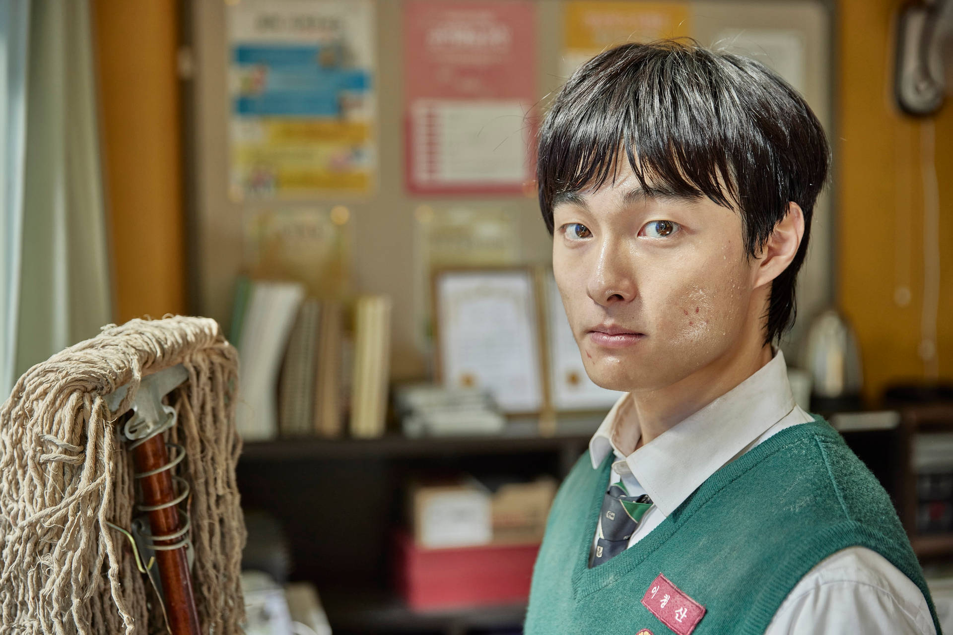 年輕男子穿綠色背心在雜亂辦公室拿拖把