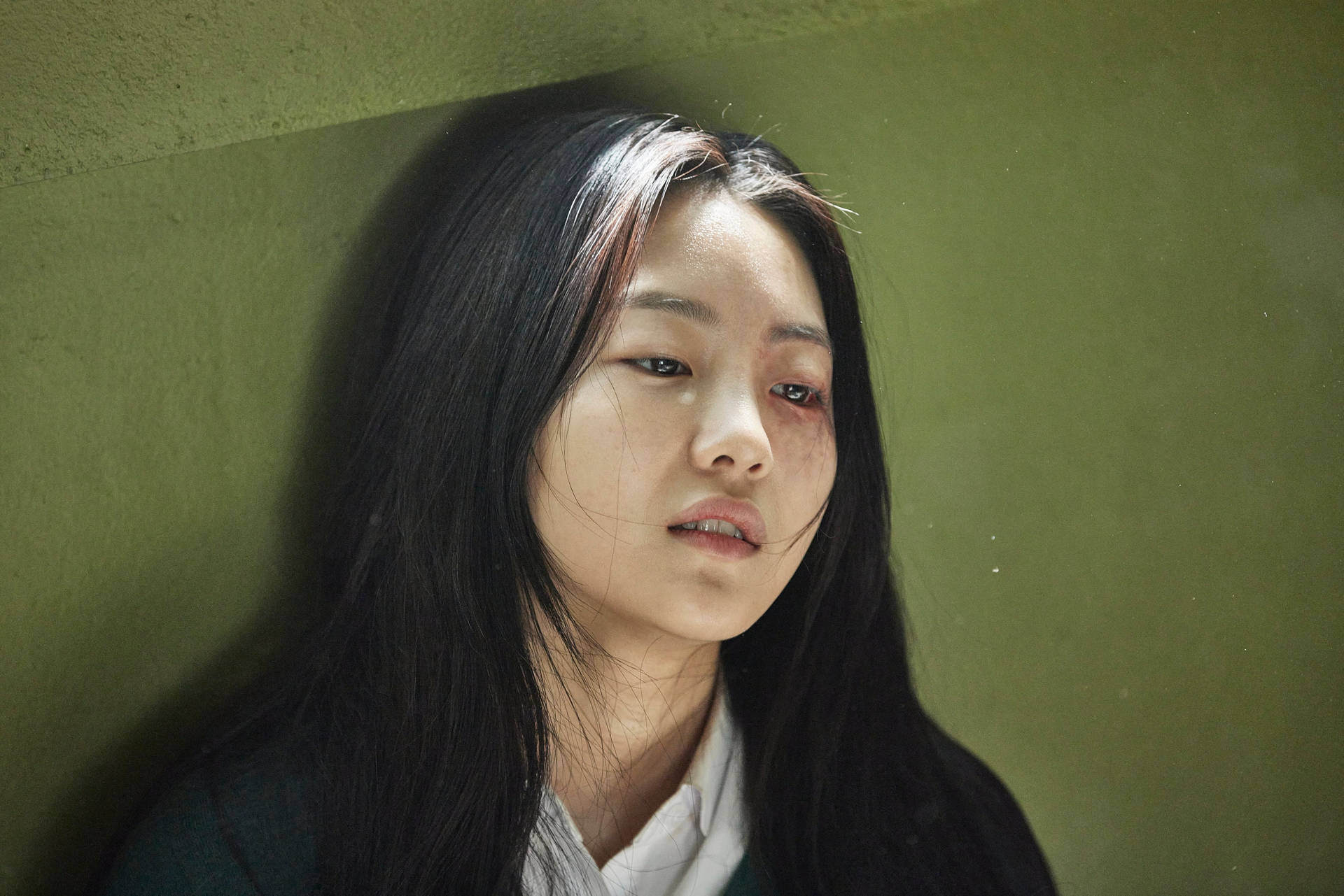 眼睛瘀傷的年輕女子靠在綠色牆上，顯得痛苦。