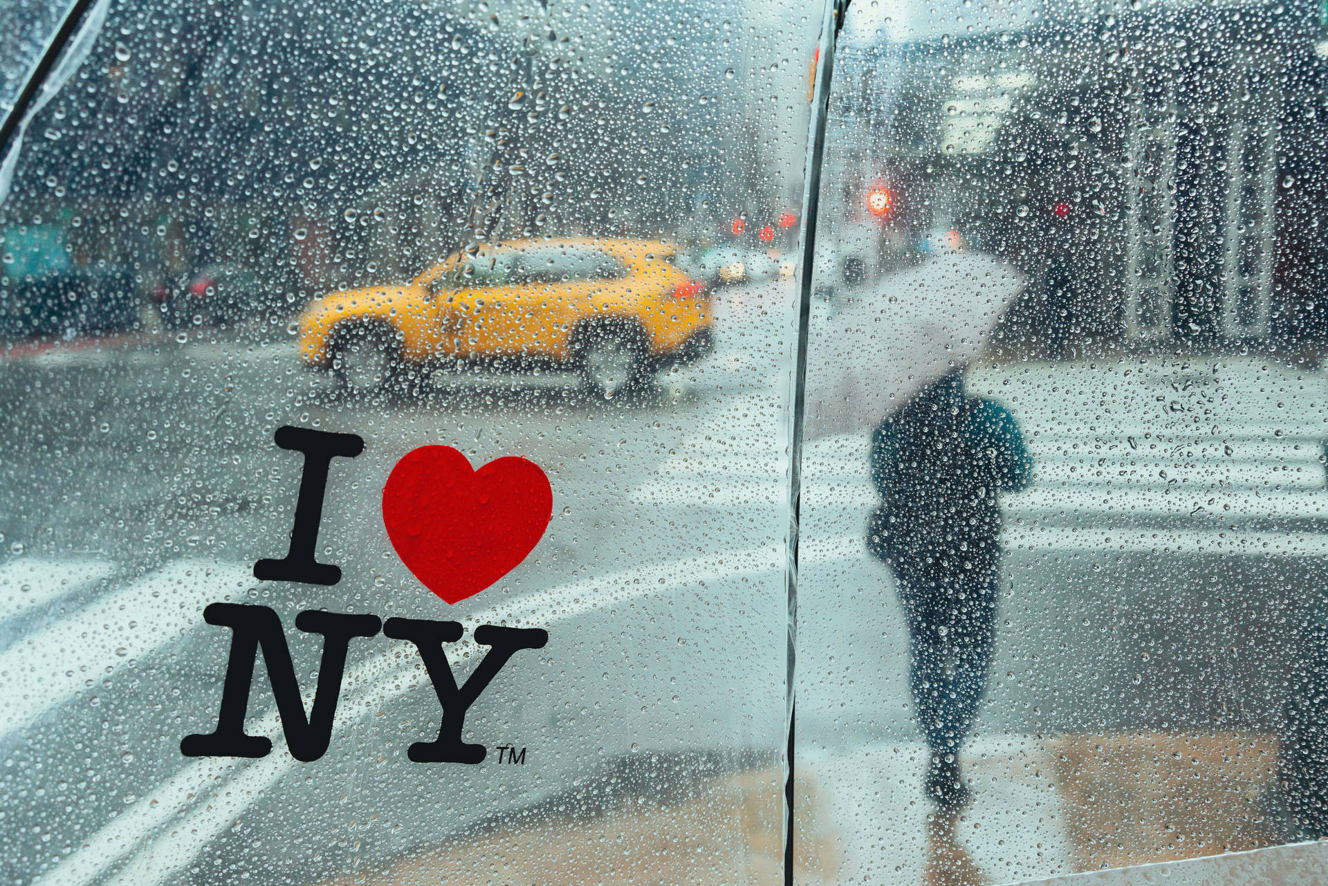 透過車窗看到的雨中城市景象，帶有 I heart NY 貼紙和黃色出租車。