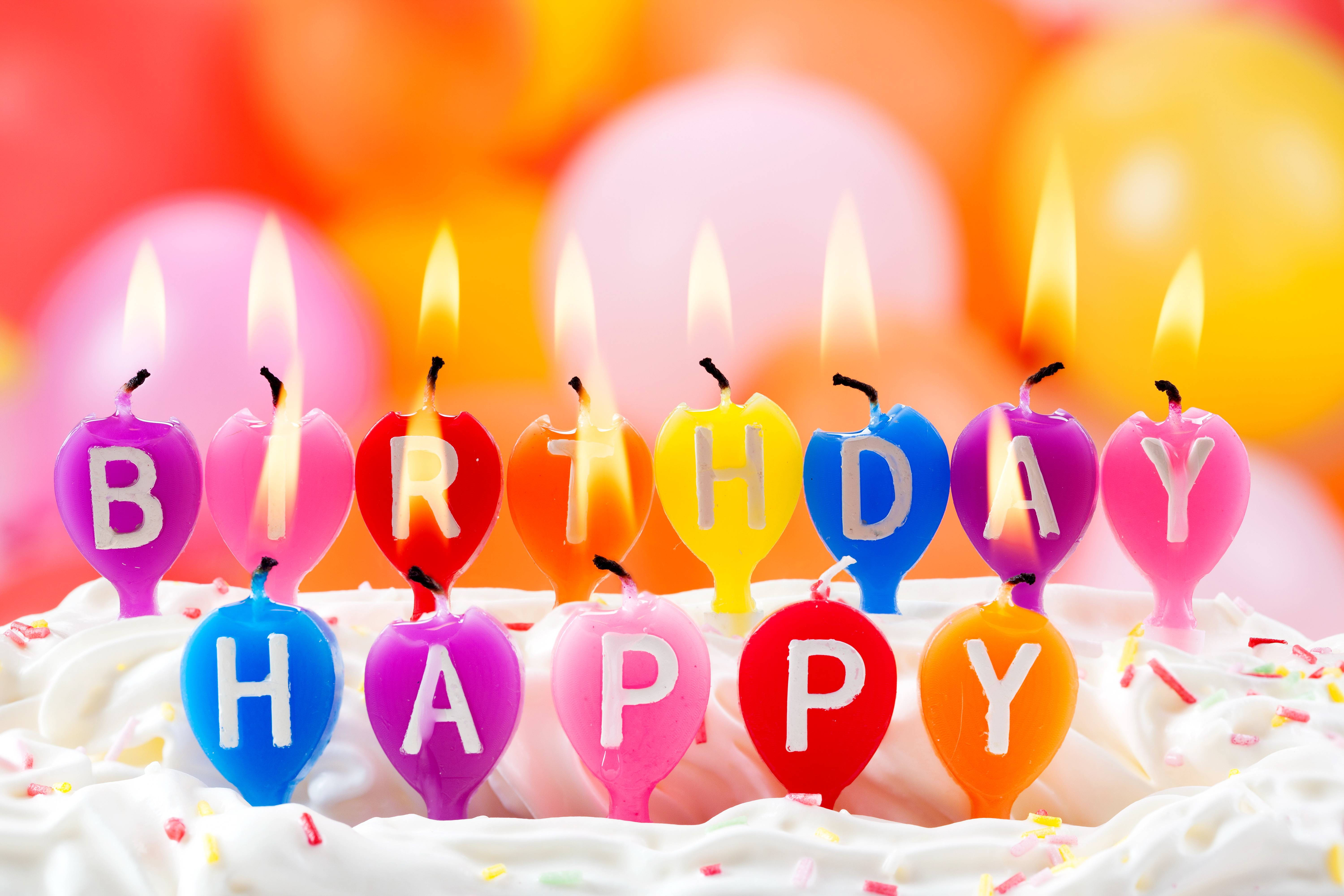 我的生日融化的蠟燭 壁紙 — 色彩繽紛的心形生日蠟燭拼出「生日快樂」，在糖霜蛋糕上閃耀，背景有糖粒和模糊的氣球。