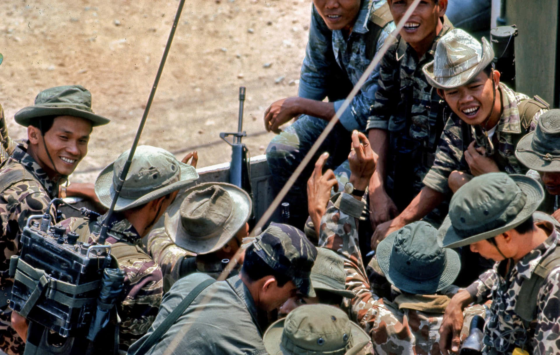穿著迷彩裝備的士兵在塵土飛揚的戶外環境中微笑互動。