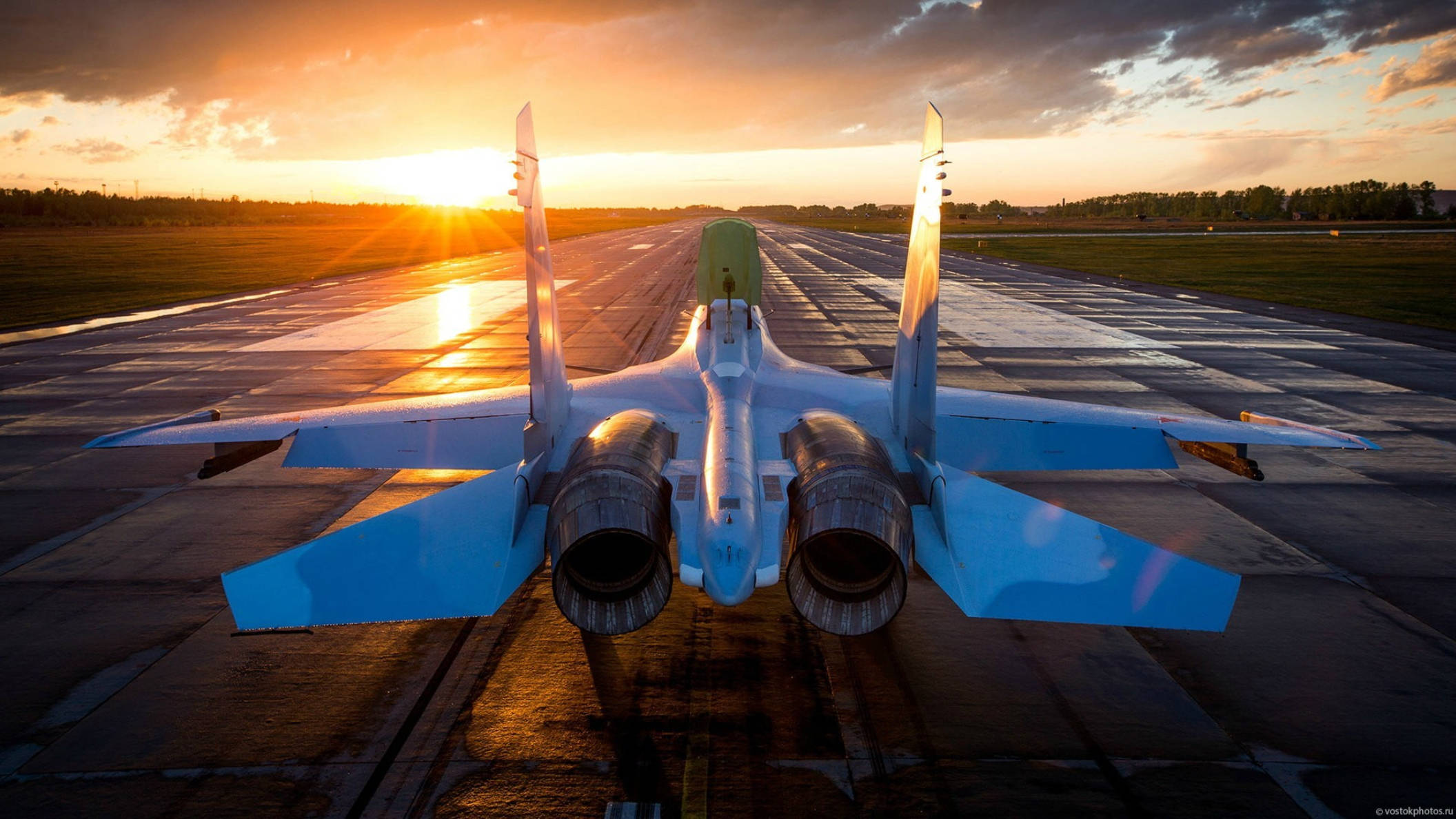 戰鬥機在跑道上 壁紙 — 一架戰鬥機停在跑道上，沐浴在金色的日落光線中，頭頂有戲劇性的雲彩。