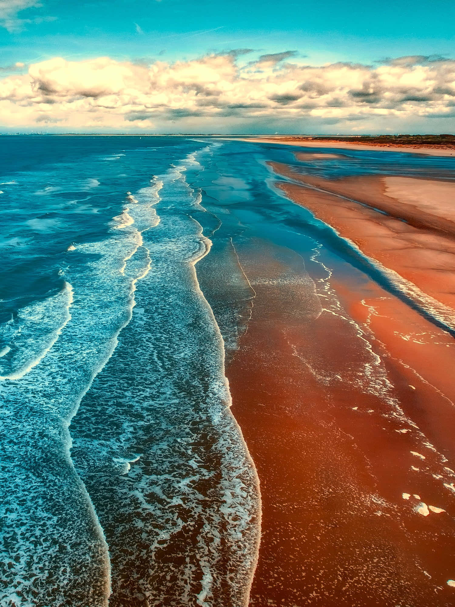 Seashore 桌布 壁紙 — 戲劇性多雲天空下，海浪拍打鮮紅色沙灘的鳥瞰圖。