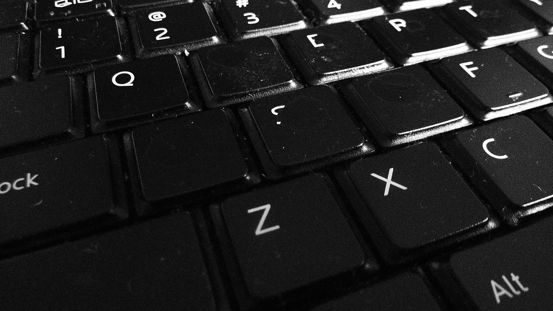 Laptop 桌布 壁紙 — 戲劇性燈光下，一個磨損的黑色鍵盤特寫，帶有白色字母。