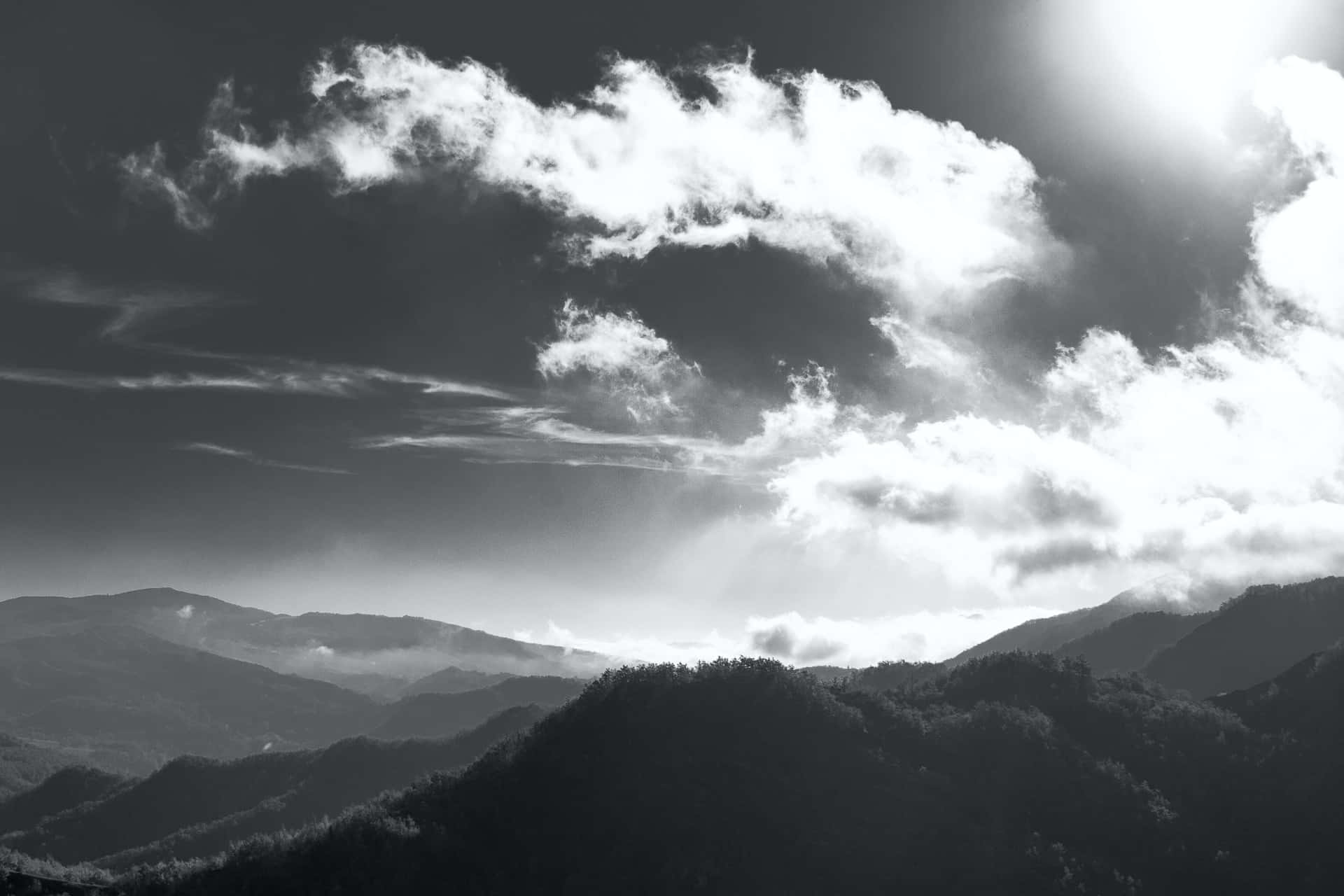 Black And White Sky 桌布 壁紙 — 戲劇性的單色山脈，帶有紋理雲層和穿透天空的陽光。