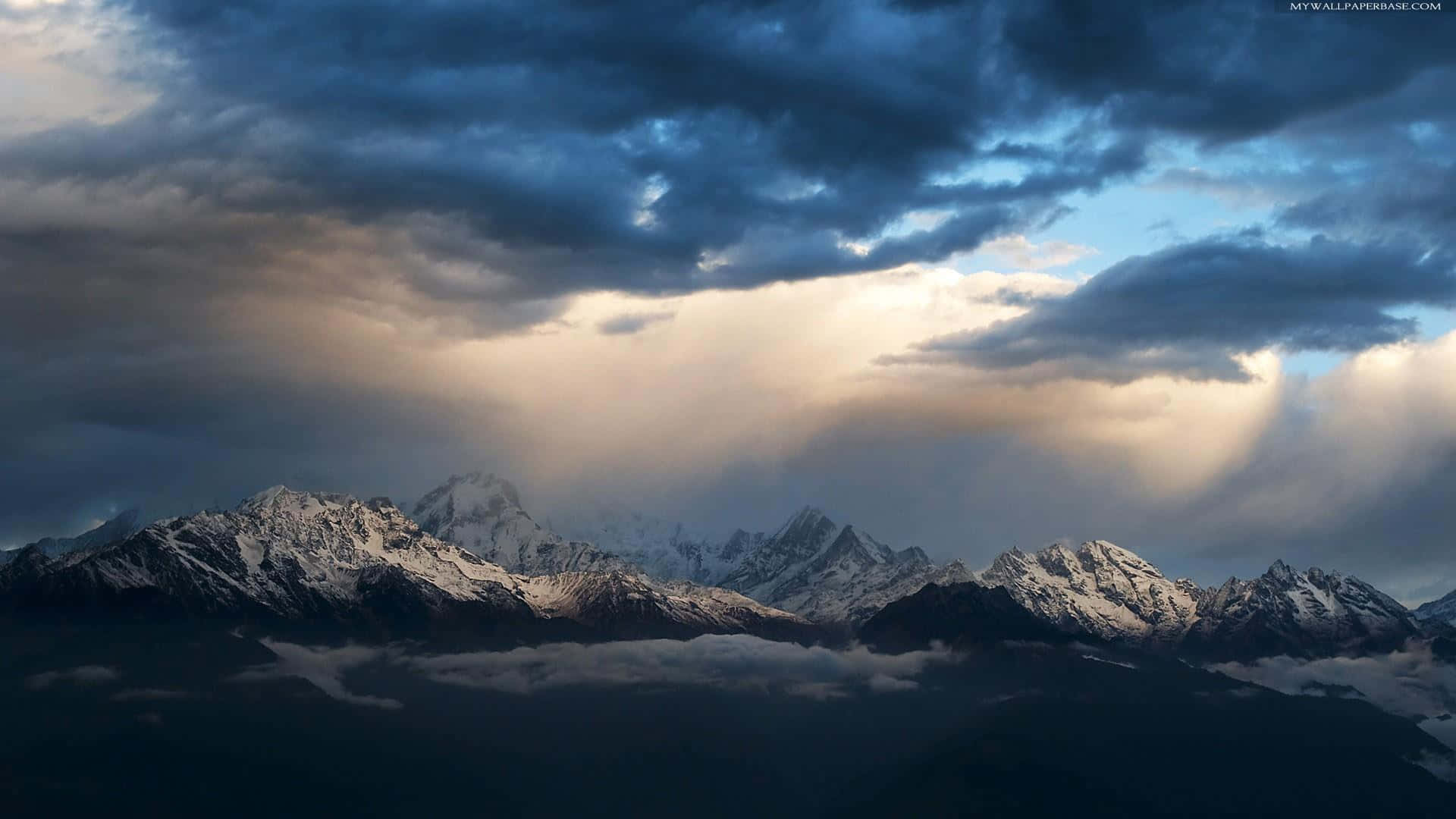 Snowstorm 桌布 壁紙 — 戲劇性的山峰刺穿暴風雲，金色陽光在霧海之上穿透而出。