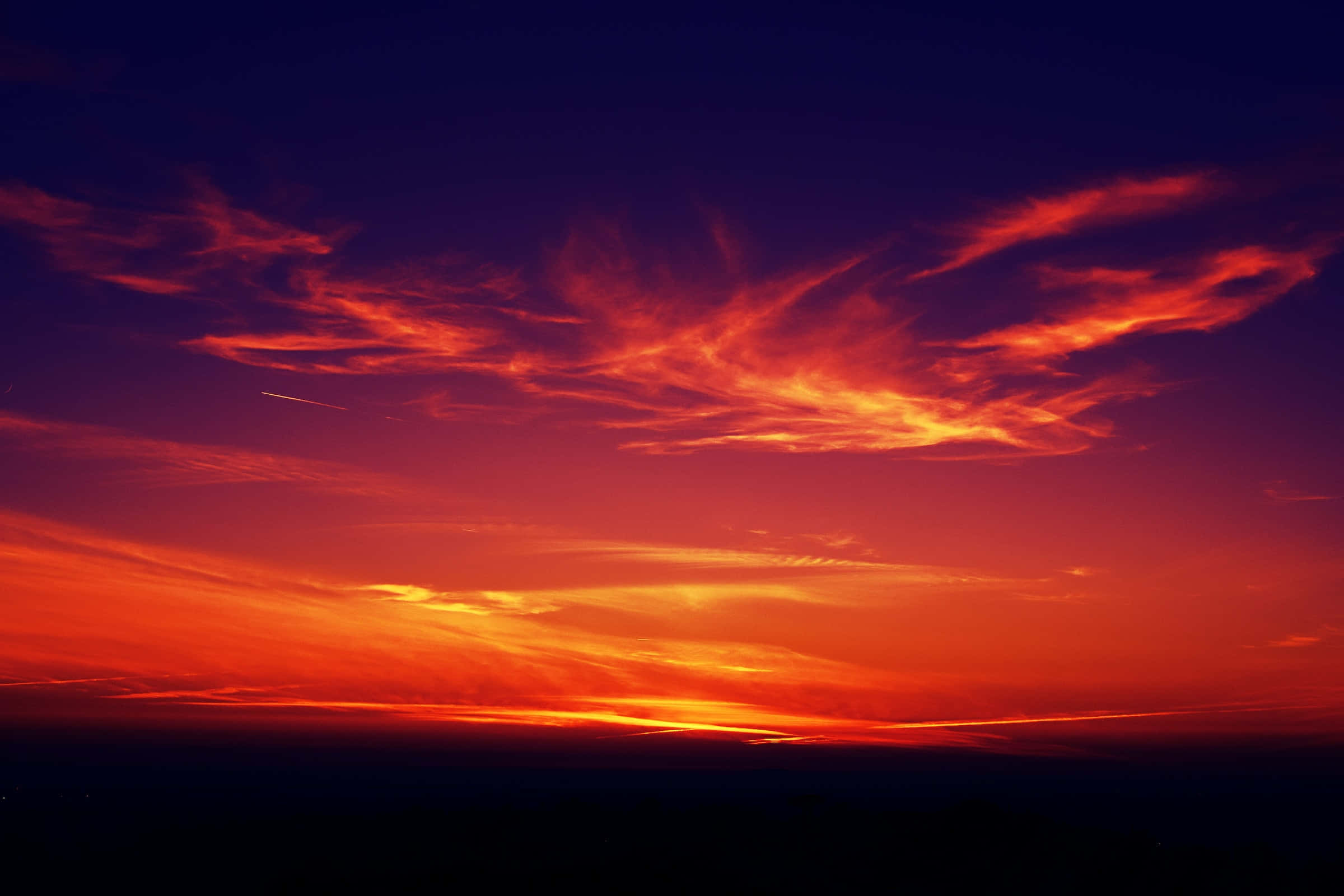 Red Sunset 桌布 壁紙 — 戲劇性的日落天空，火熱的橙色和深紫色雲彩在黑暗的地平線上燃燒。