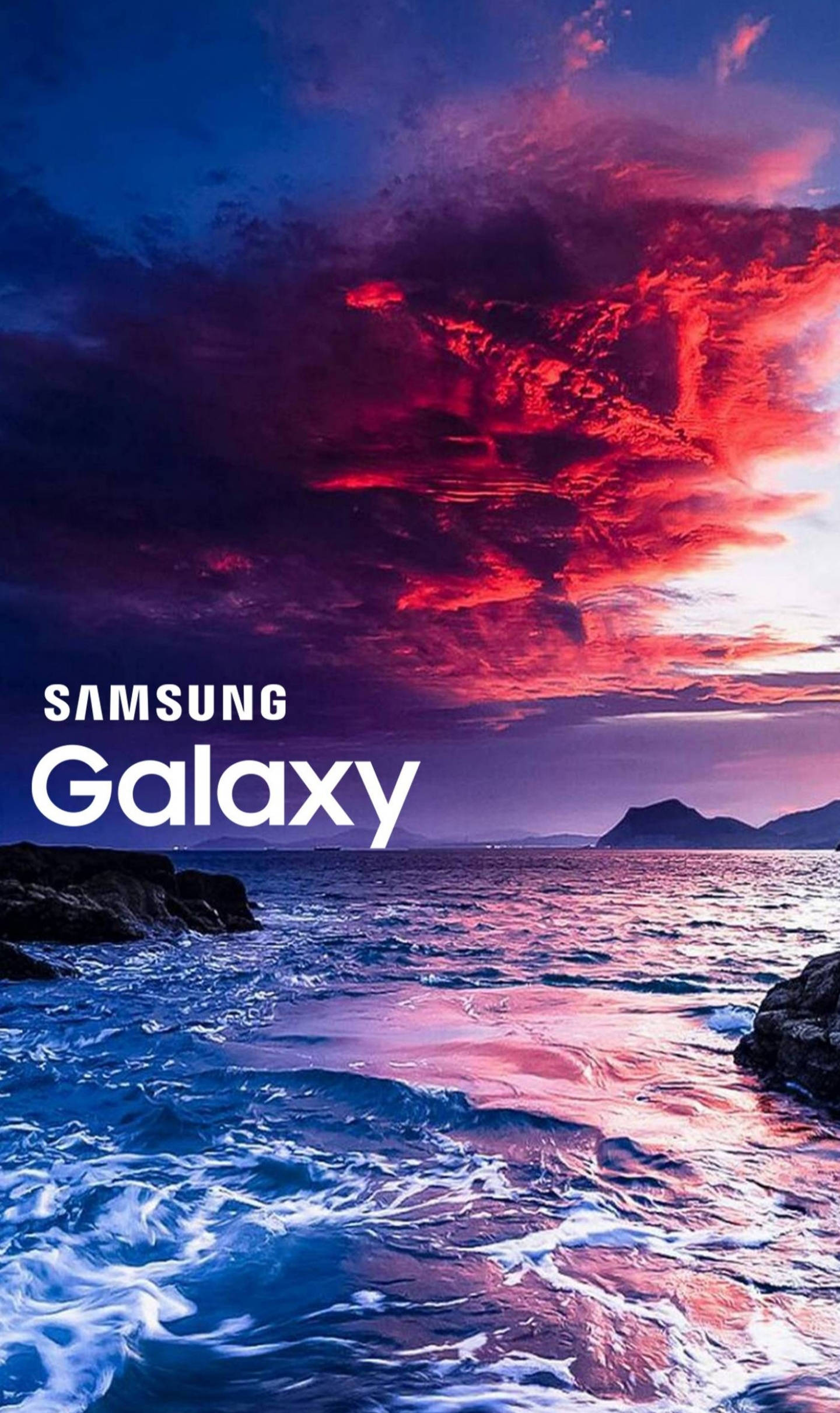 Ocean Sunset 桌布 壁紙 — 戲劇性的日落將天空染成火紅和深藍，映照在波濤洶湧的海洋和岩石海岸上。