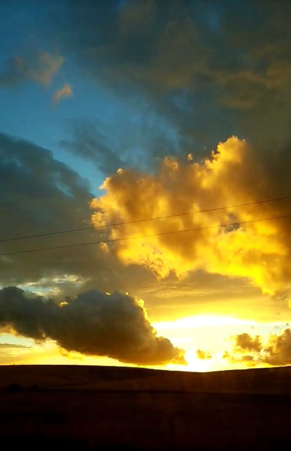 Yellow Sky 桌布 壁紙 — 戲劇性的日落將雲彩染成火熱的金色，映襯著剪影地平線之上的深藍色天空。