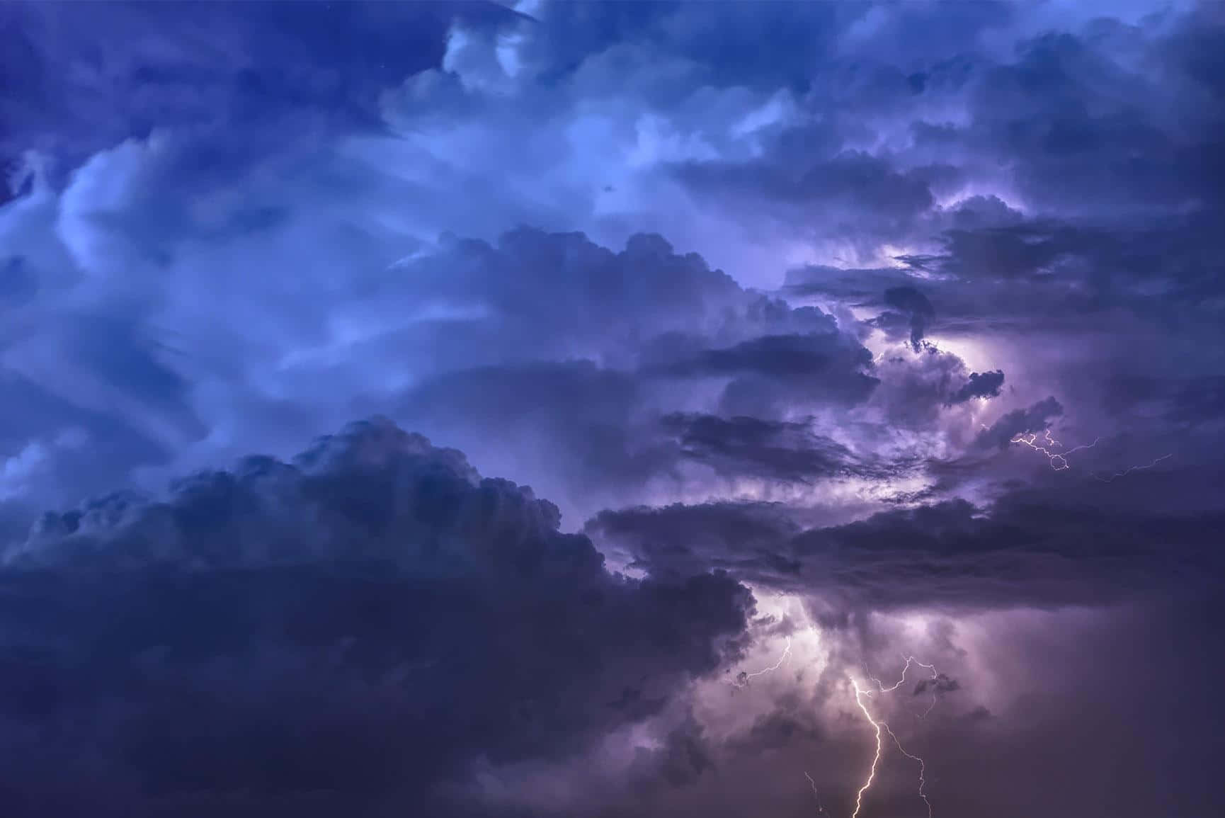 唯美雲朵 桌布 壁紙 — 戲劇性的暴風雨天空，深紫色和藍色的雲層被鮮明的閃電照亮。