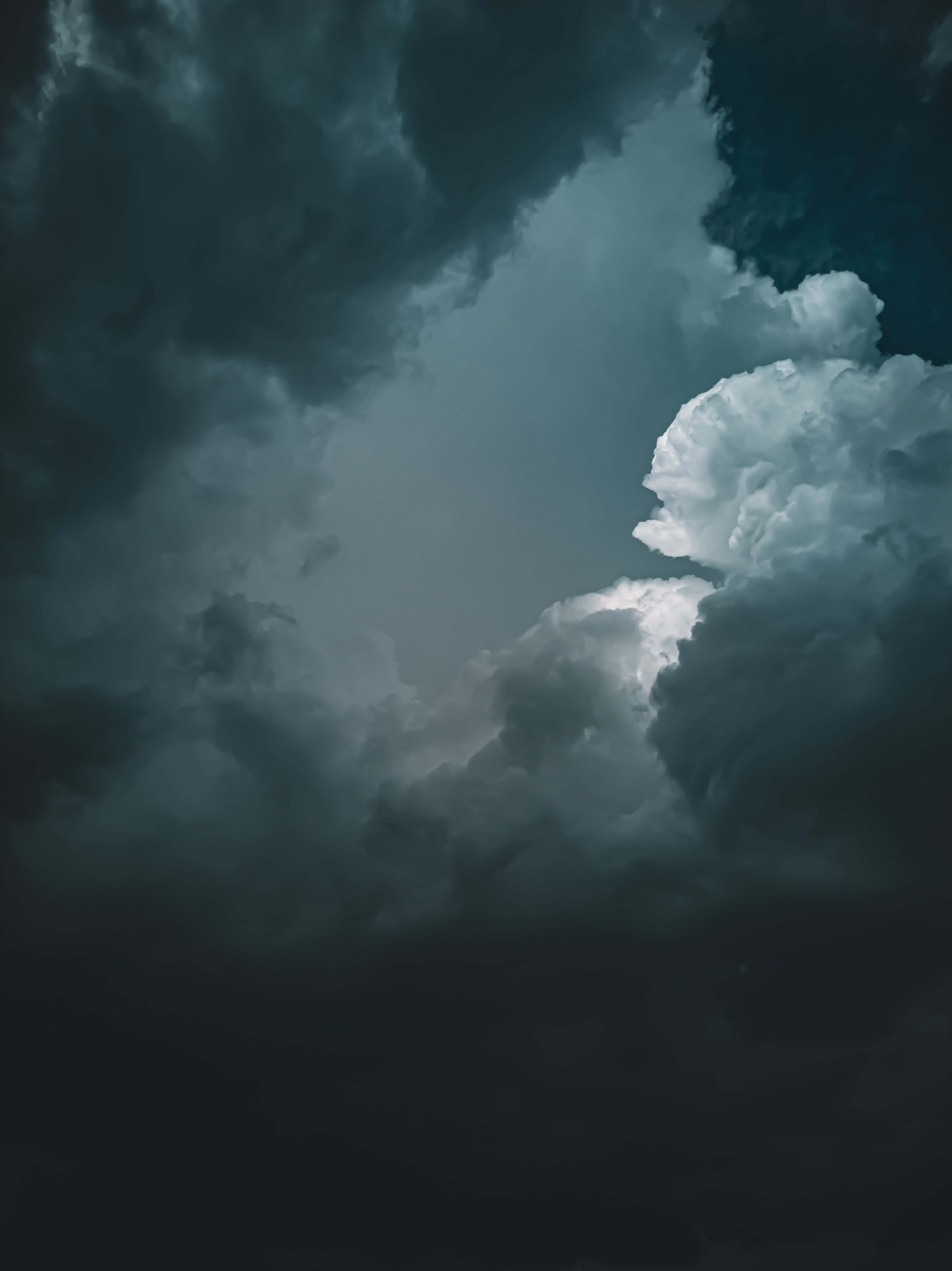 Dark Heaven 桌布 壁紙 — 戲劇性的暴風雲以深藍綠色和灰色調旋轉，一縷明亮的雲朵劃破陰暗。