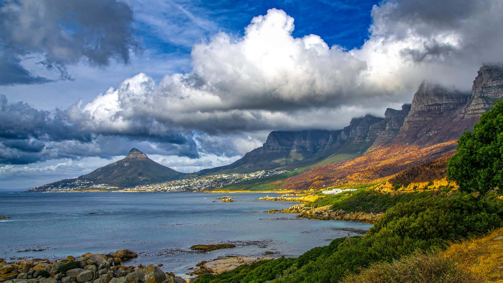 South Africa 桌布 壁紙 — 戲劇性的海岸山脈在平靜的海灣後方升起，天空佈滿大膽的白色和灰色雲朵。