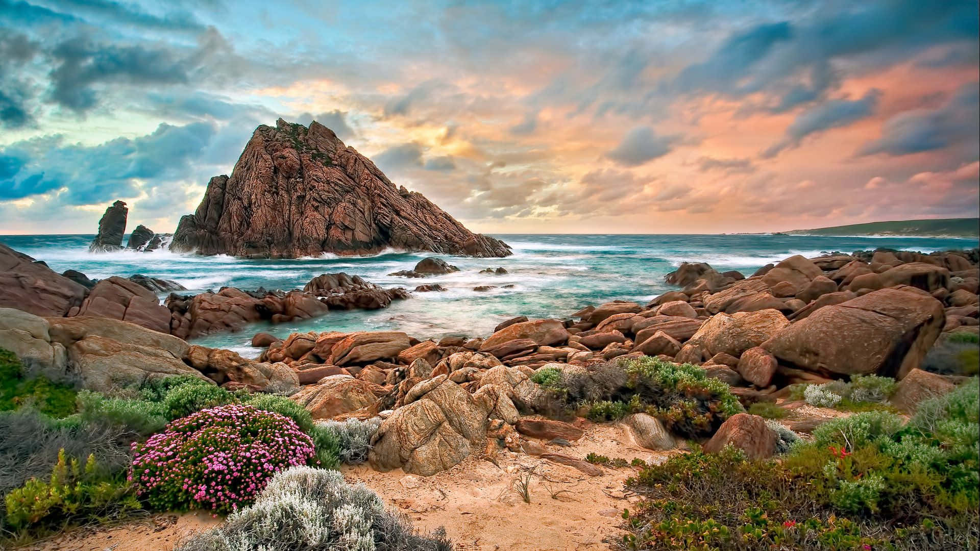 Australia Beach 桌布 壁紙 — 戲劇性的海岸景色，有崎嶇的紅色岩石、翻騰的碧綠海浪和充滿活力的日落天空。