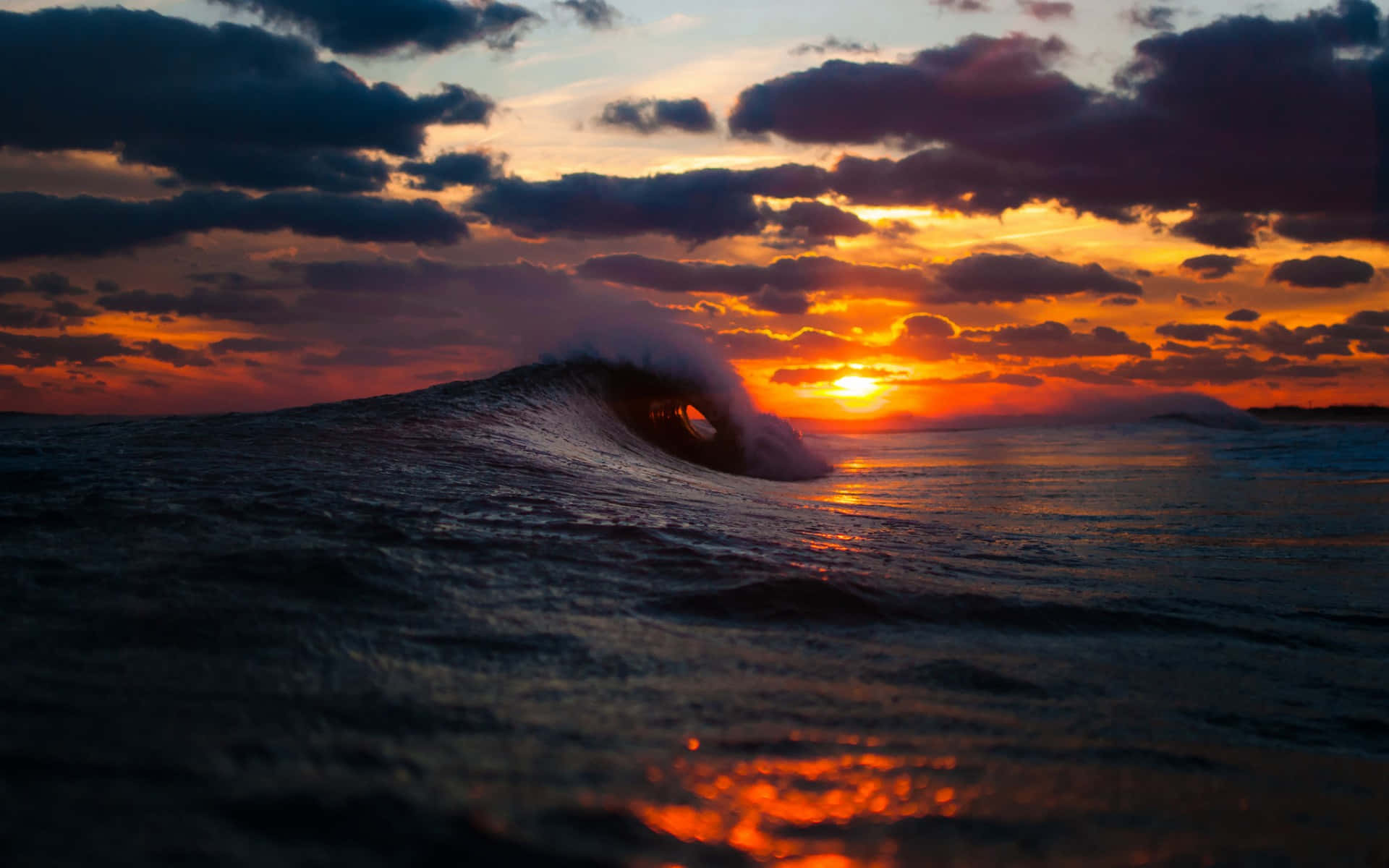 Sunset Ocean 桌布 壁紙 — 戲劇性的海浪在日落時翻捲，上方有火橙色和紫色的雲彩。