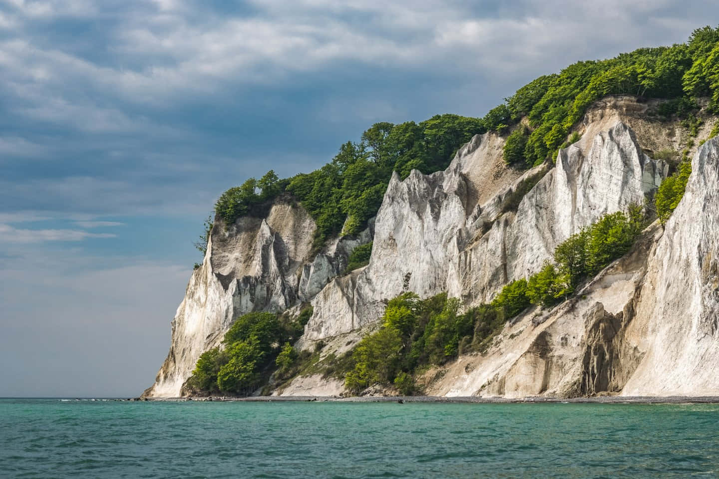 Nature Scenery 桌布 壁紙 — 戲劇性的白色懸崖，覆蓋著茂密的綠色樹木，從平靜的碧綠海水中升起，天空多雲。