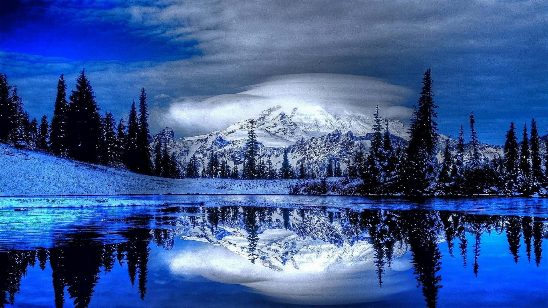 冬天桌面 桌布 壁紙 — 戲劇性的藍天下，白雪覆蓋的山峰完美地倒映在平靜的冰湖中，四周環繞著常青樹。