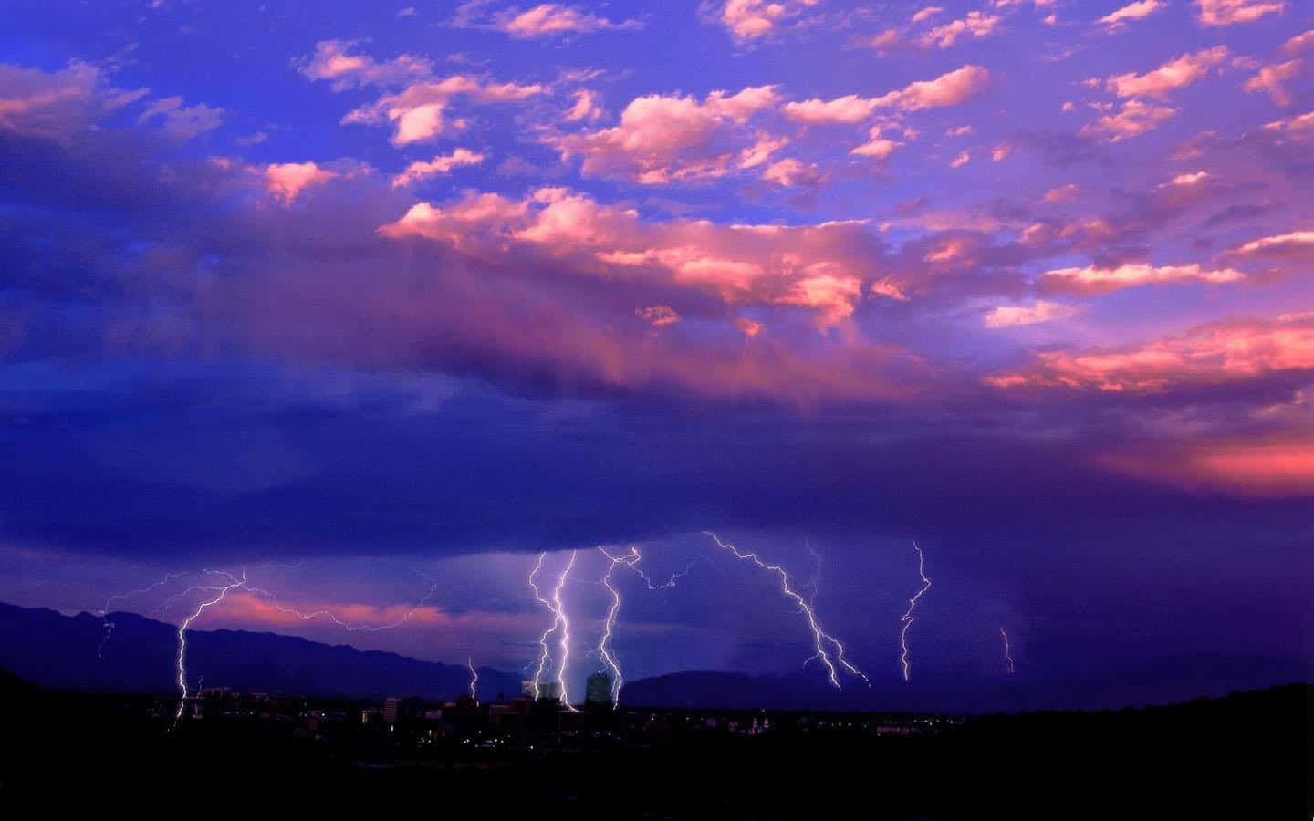 Thunderstorm 桌布 壁紙 — 戲劇性的閃電照亮了黃昏時分山脈和城市景觀剪影上方暴風雨的紫色和粉紅色天空。