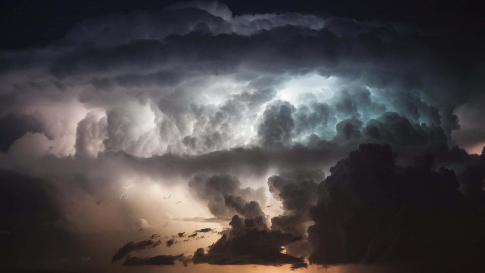 Thunderstorm 桌布 壁紙 — 戲劇性的風暴雲層形成，被閃電和日落色調照亮，投射出不祥的光芒。