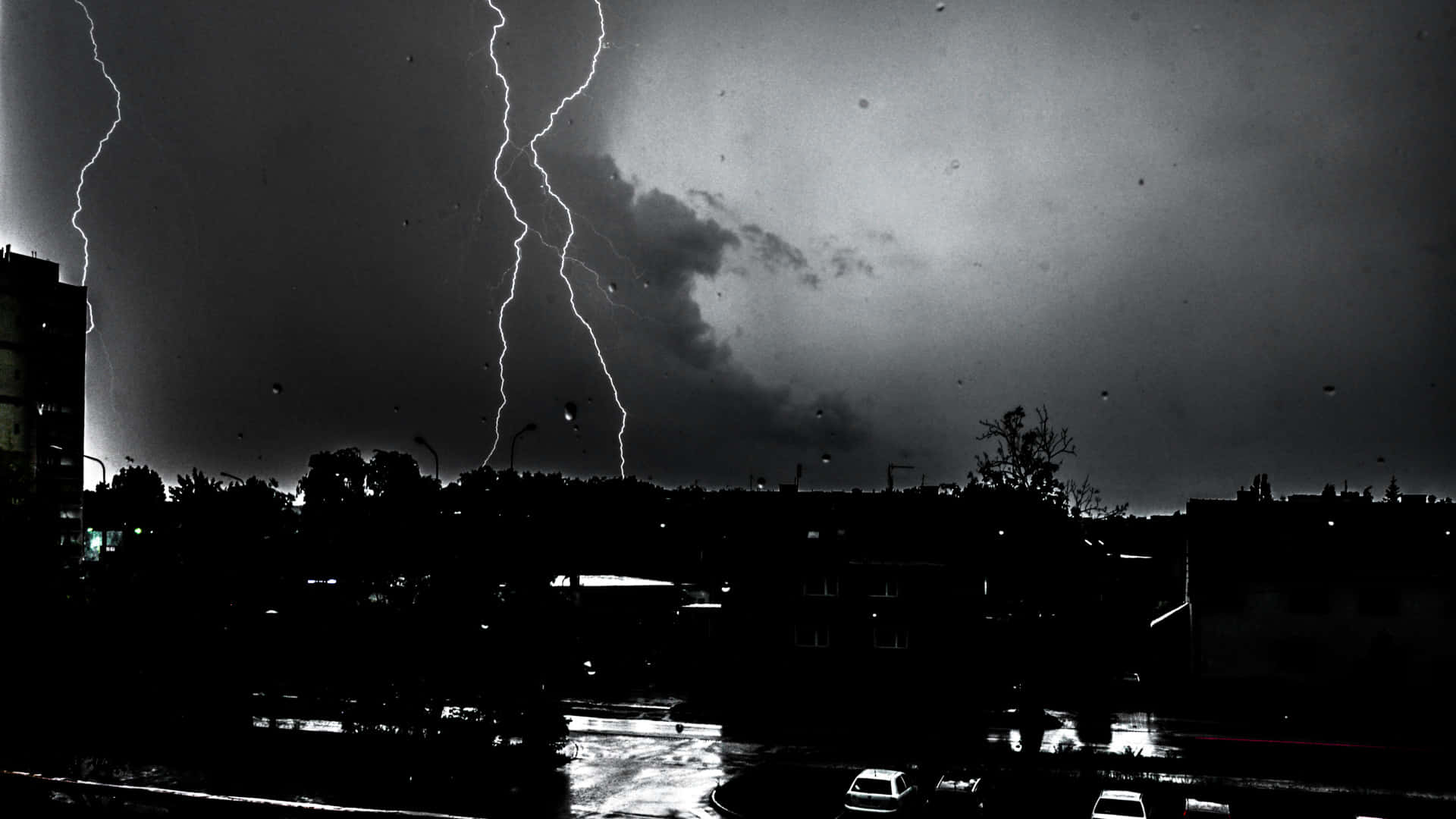 Black And White Storm 桌布 壁紙 — 戲劇性的黑白閃電照亮了濕漉漉的街道和剪影建築上方的暴風雨城市天際線。