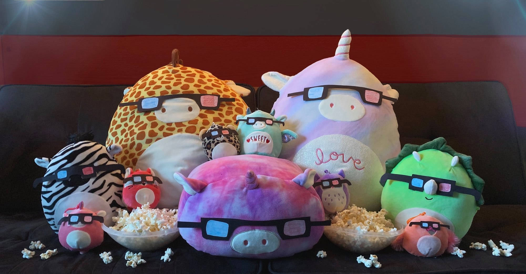 戴3D眼鏡的Squishmallows玩偶 壁紙 — 一群色彩繽紛的毛絨玩具戴著3D眼鏡，坐在沙發上，旁邊有爆谷碗。