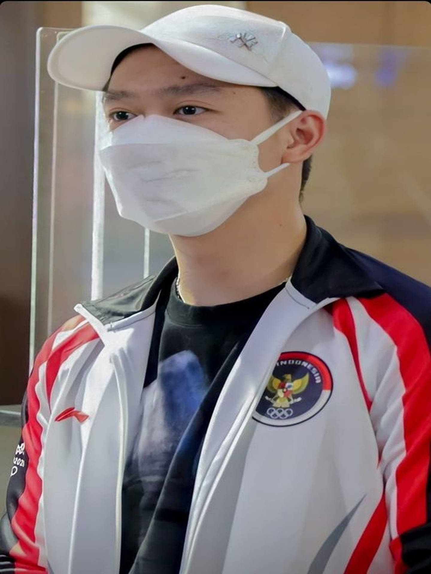 年輕印尼運動員戴口罩和隊服夾克站在屏障後