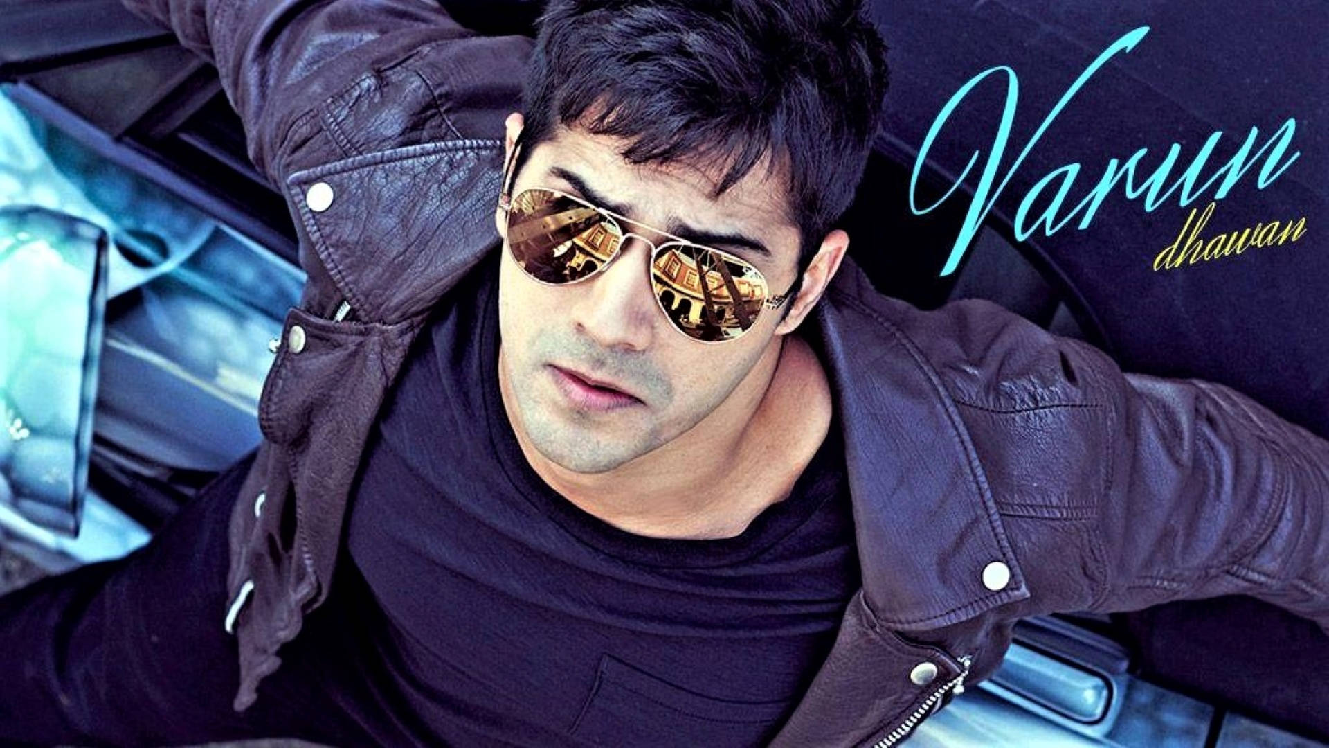 戴墨鏡的帥哥 Varun Dhawan 壁紙 — 一名身穿皮褸和反光飛行員太陽眼鏡的男子，在車內自信地放鬆，車內有風格化的名字疊加。