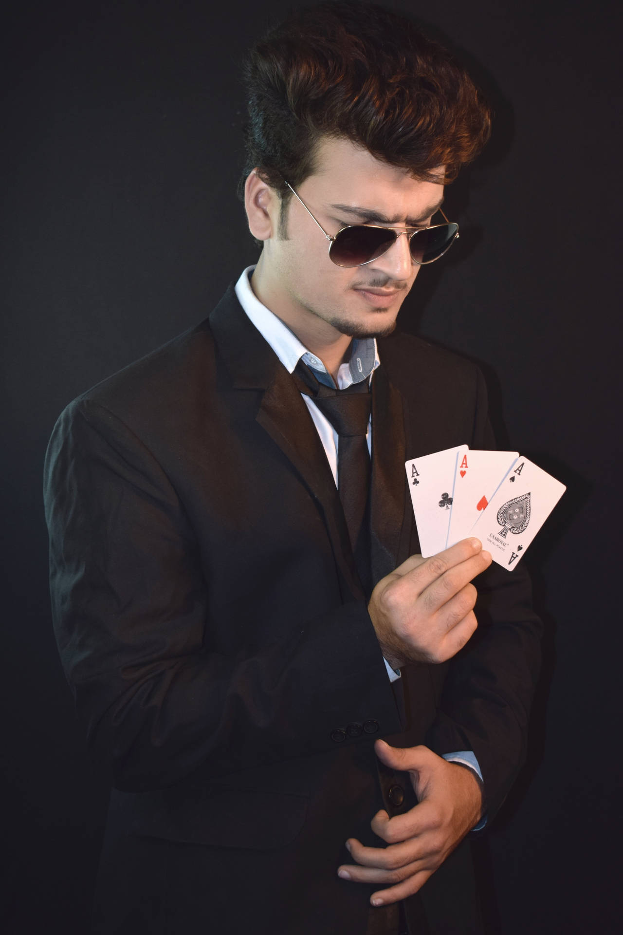 穿西裝和太陽眼鏡的男士在昏暗的攝影棚中手持三張Ace。