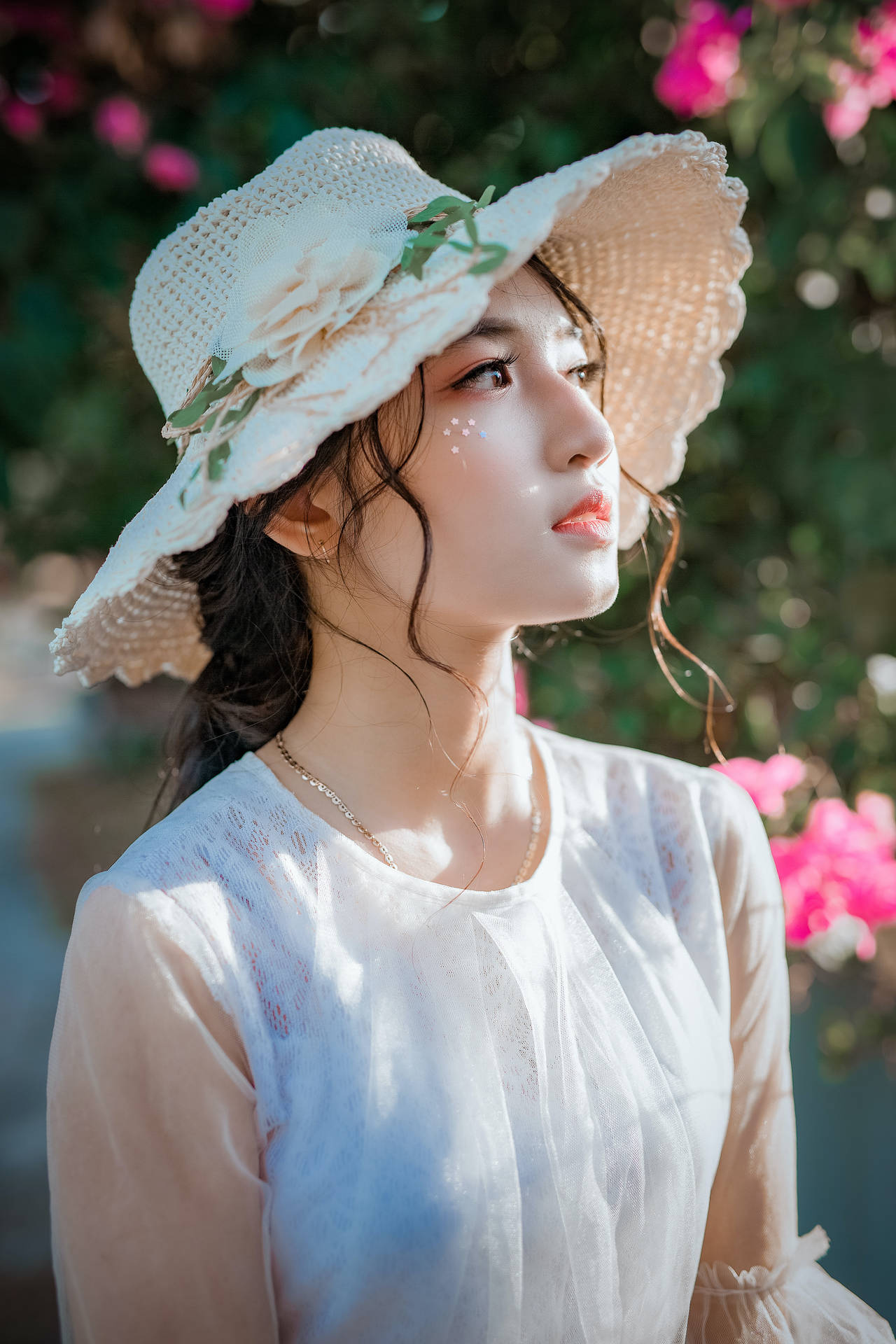 戴白色帽子和襯衫的女子站在陽光下的粉紅色花朵中。