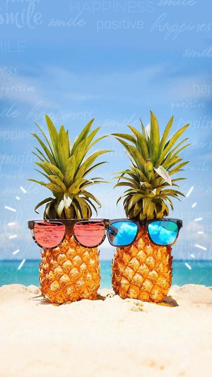 戴太陽眼鏡的可愛夏日海灘鳳梨 壁紙 — 兩個戴著彩色太陽眼鏡的菠蘿站在陽光明媚的海灘上，背景是海洋和天空。