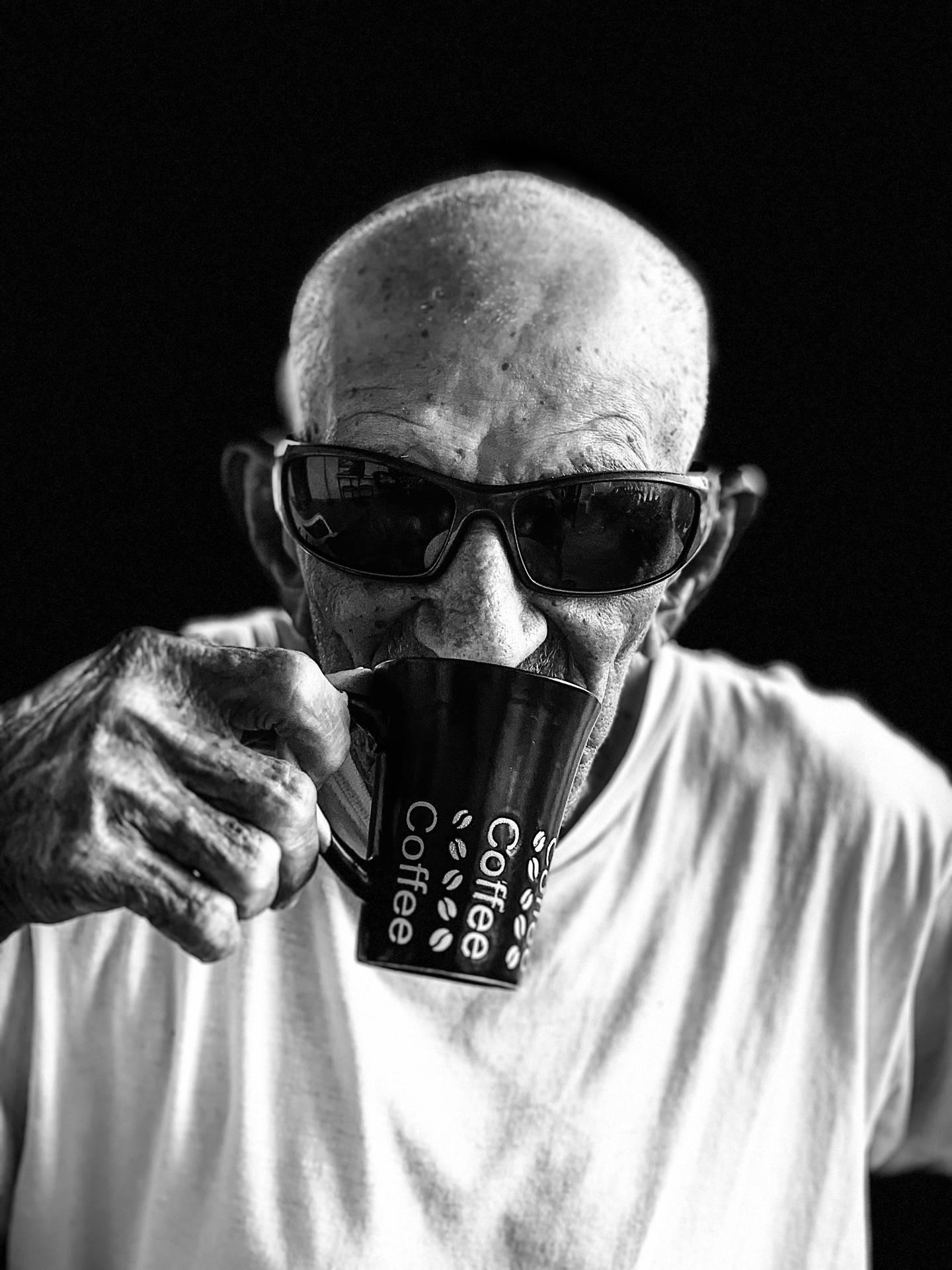 一位戴太陽眼鏡的長者男士以黑白風格從咖啡杯飲用。