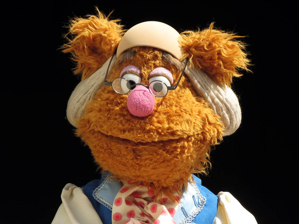 戴奶奶眼鏡的 Fozzie Bear 壁紙 — Miss Piggy 近照，身穿護士服，戴眼鏡，粉紅色鼻子，黑色背景。