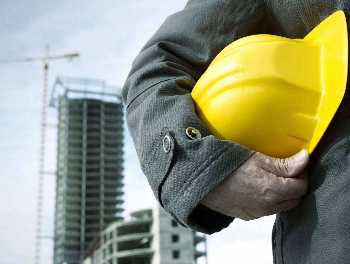 一名建築工人在興建中的高樓前手持黃色安全帽。