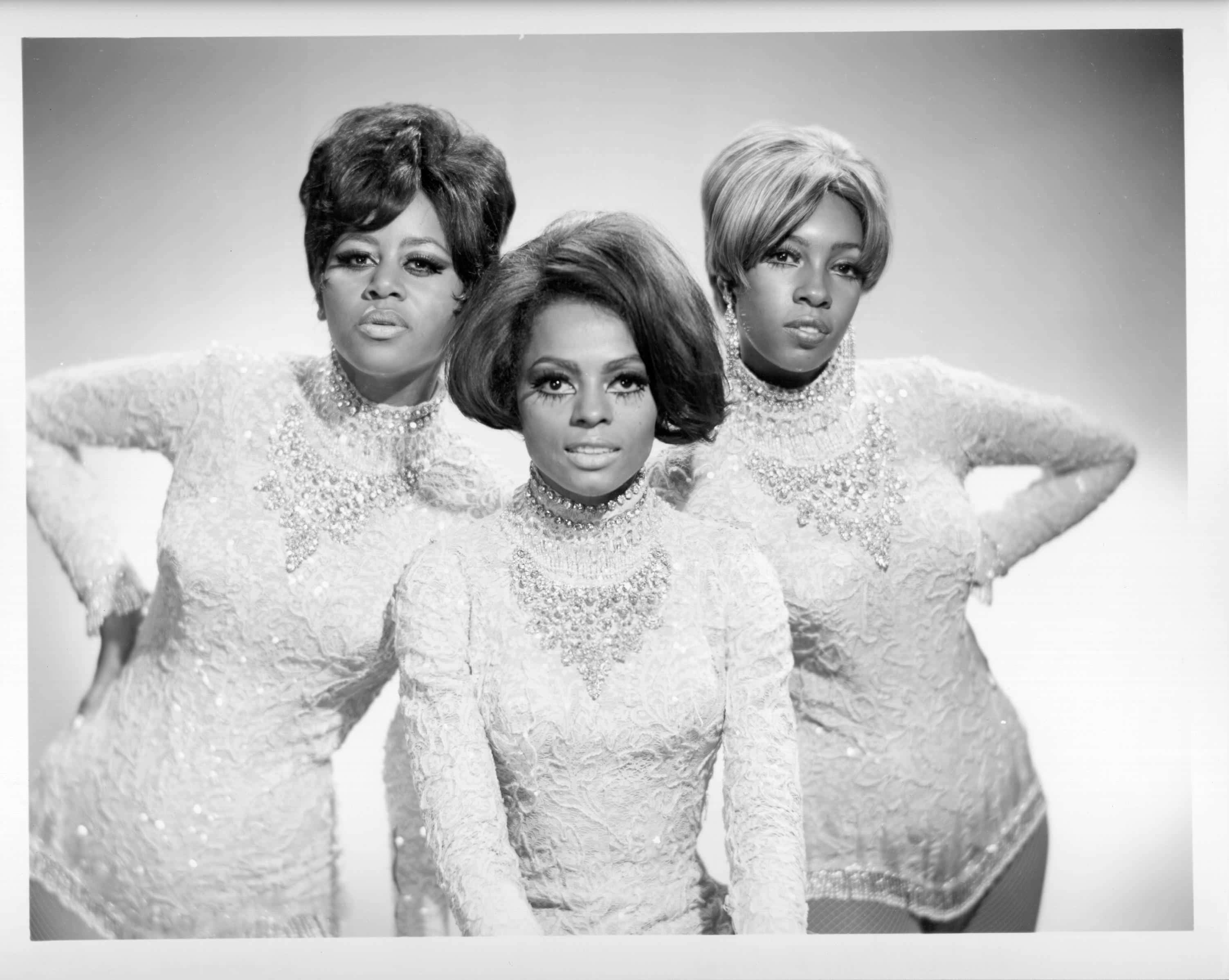 戴安娜·羅斯與The Supremes 1960 壁紙 — 三位迷人女性身穿閃亮白色服裝，在樸素的工作室背景前自信地擺姿勢。